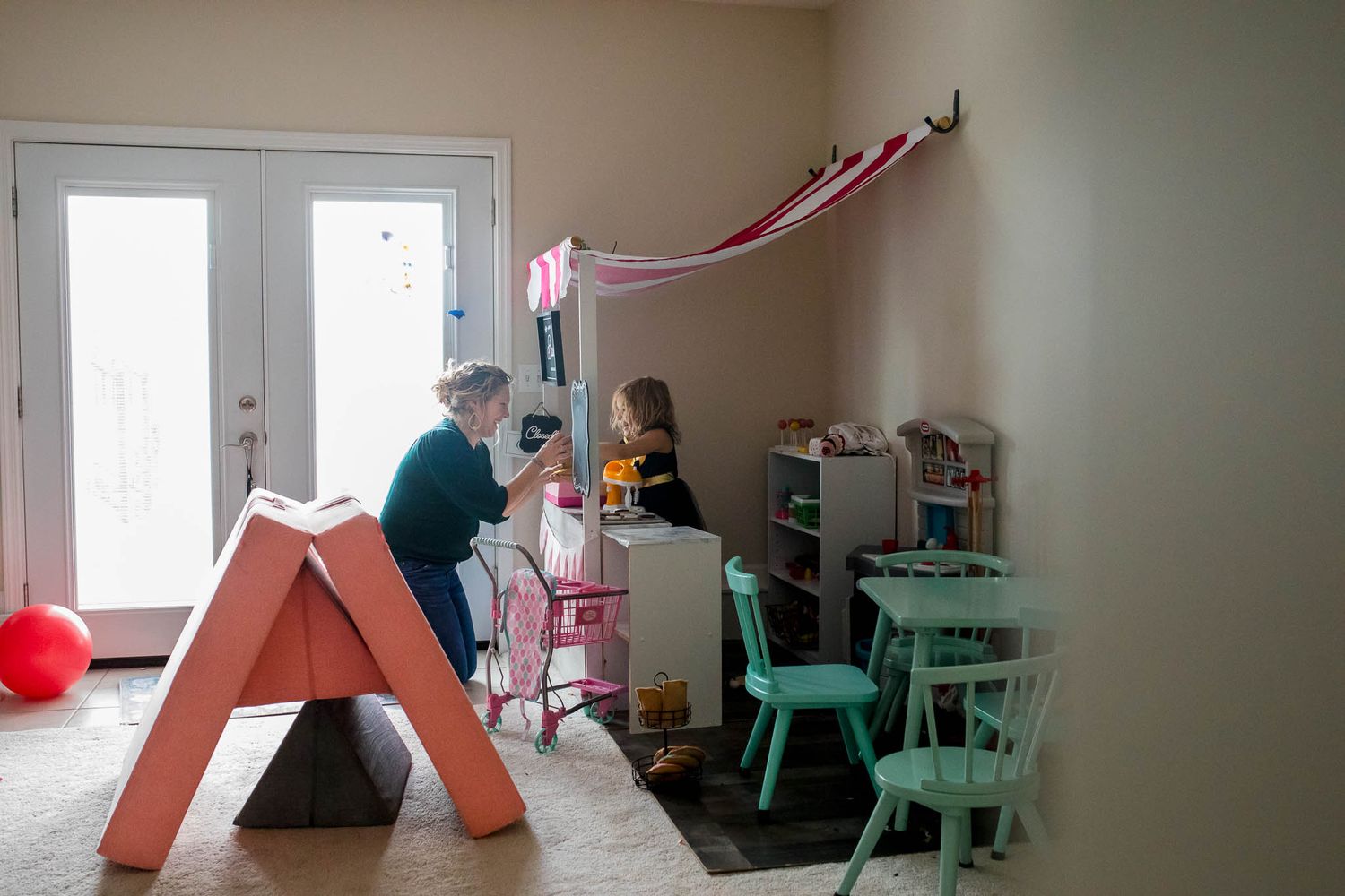 A playroom decorated with pink streamers and colorful furniture including a coral-colored slide and mint green chairs.