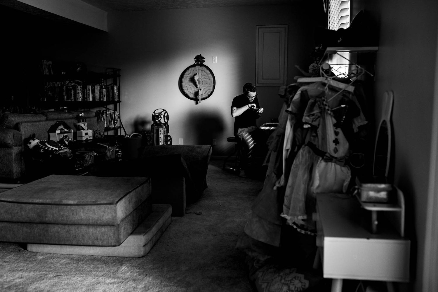 A dark moody room with coats hanging and silhouettes cast on the wall with dramatic lighting effects and shadows.