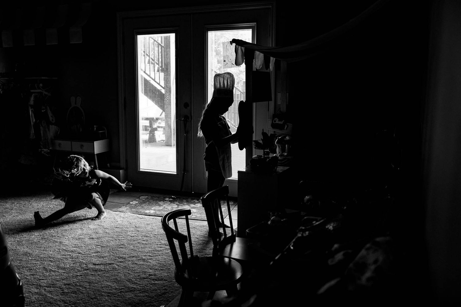 A silhouetted figure stands in a doorway while sunlight streams into a dark room.