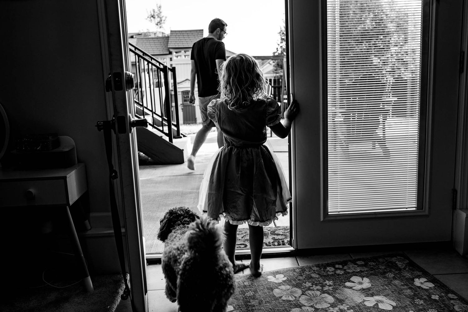A silhouetted view through glass doors showing people and a dog on an outdoor patio.