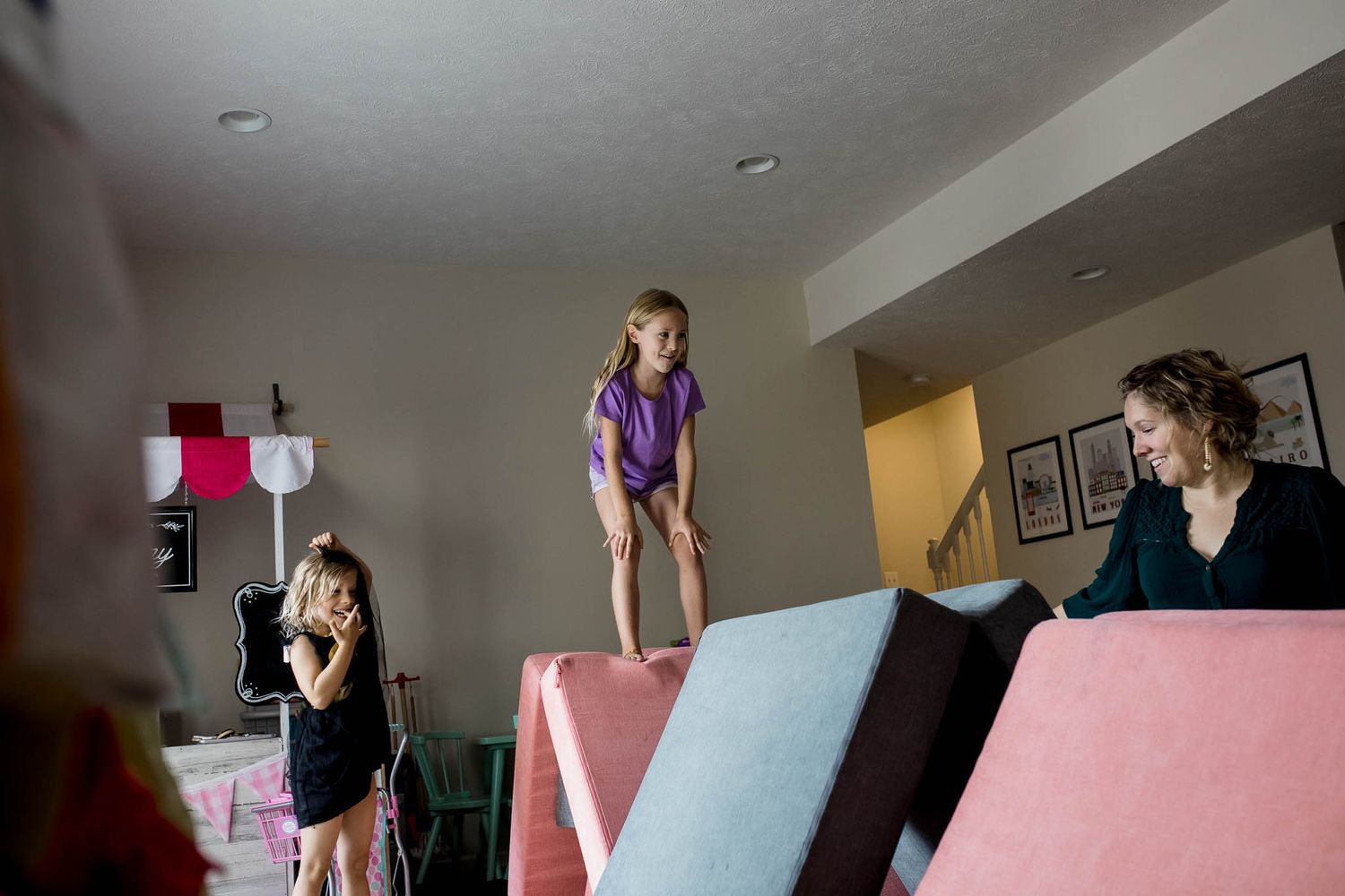 Young children jump and play on a pink couch in a living room setting.