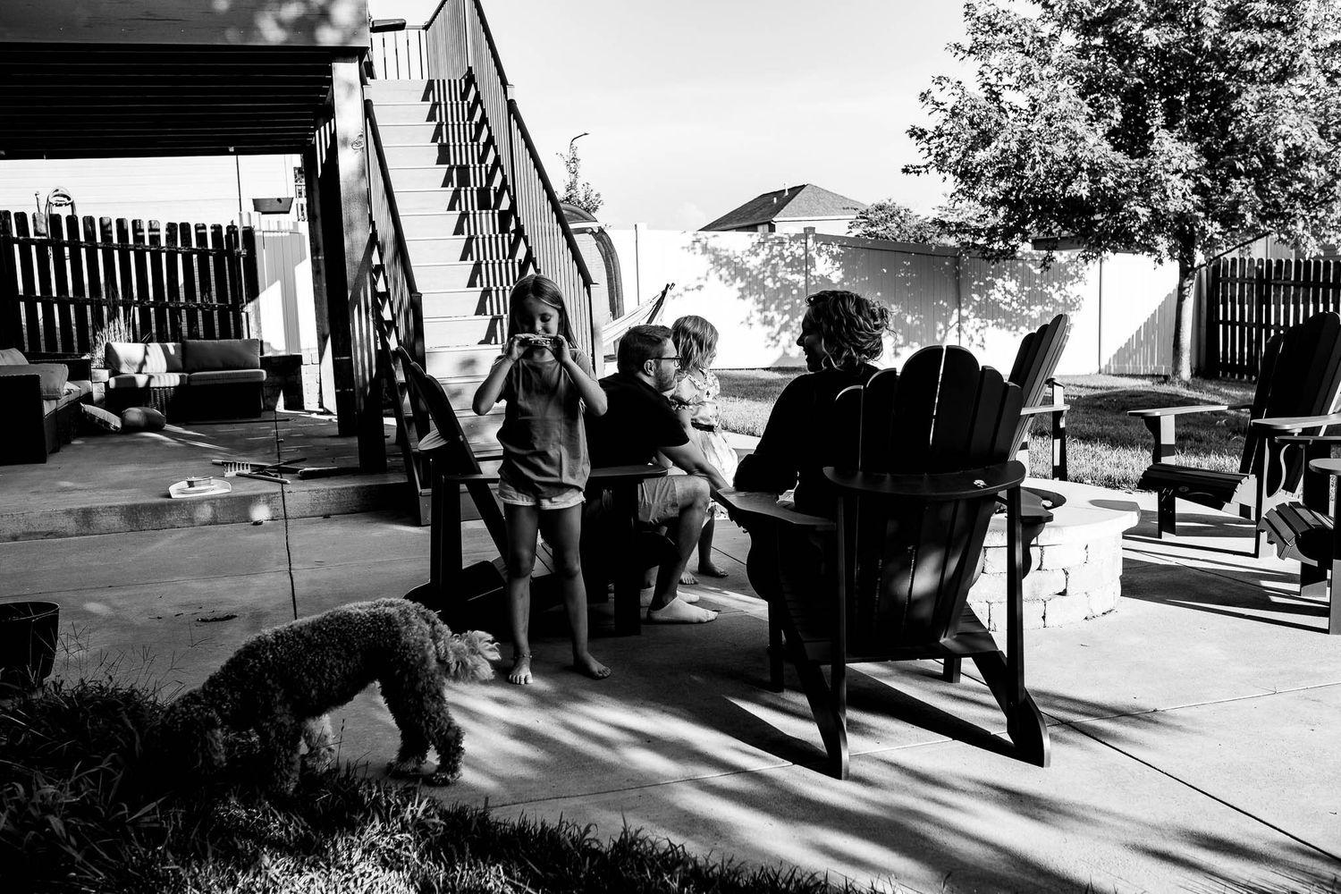Family members gather on a sunny backyard patio with outdoor furniture and stairs.