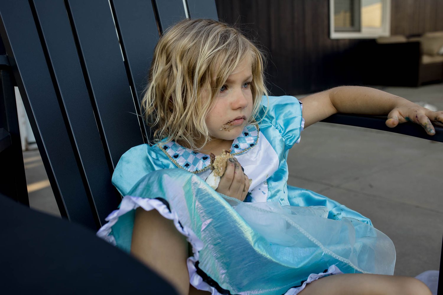 A child in a light blue dress sits on a dark wooden bench.