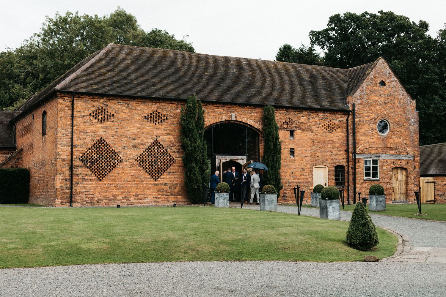 Historic brick barn venue with diamond pattern brickwork and guests gathered outside at oak farm near Ledbury, England.