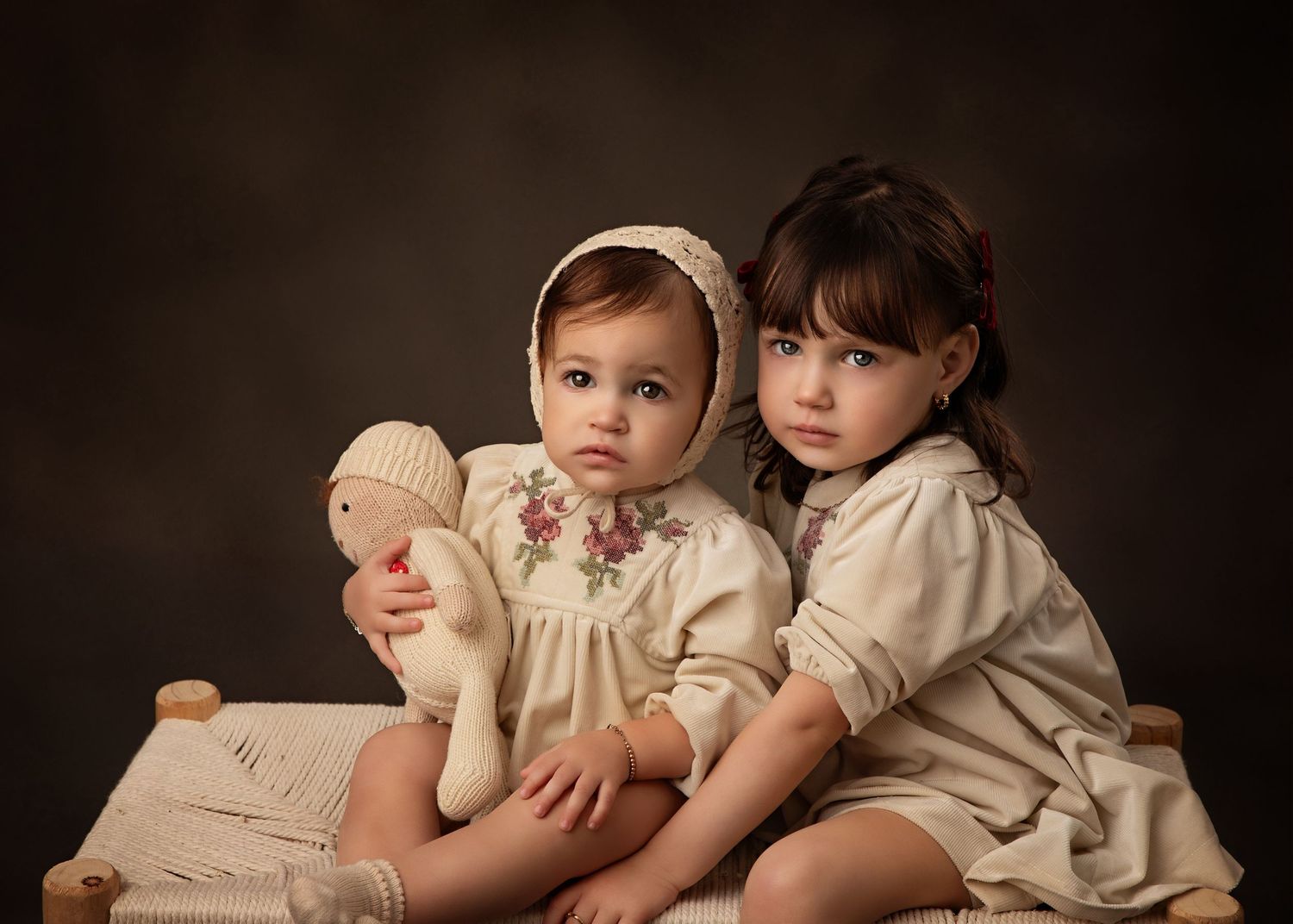 Two children in vintage white clothing pose with a stuffed lamb against a dark background.