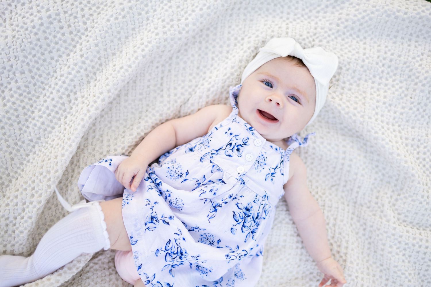 Central Illinois family photographer captures a baby girl with a bow laying on a blanket smiling during a photo session in Springfield, IL