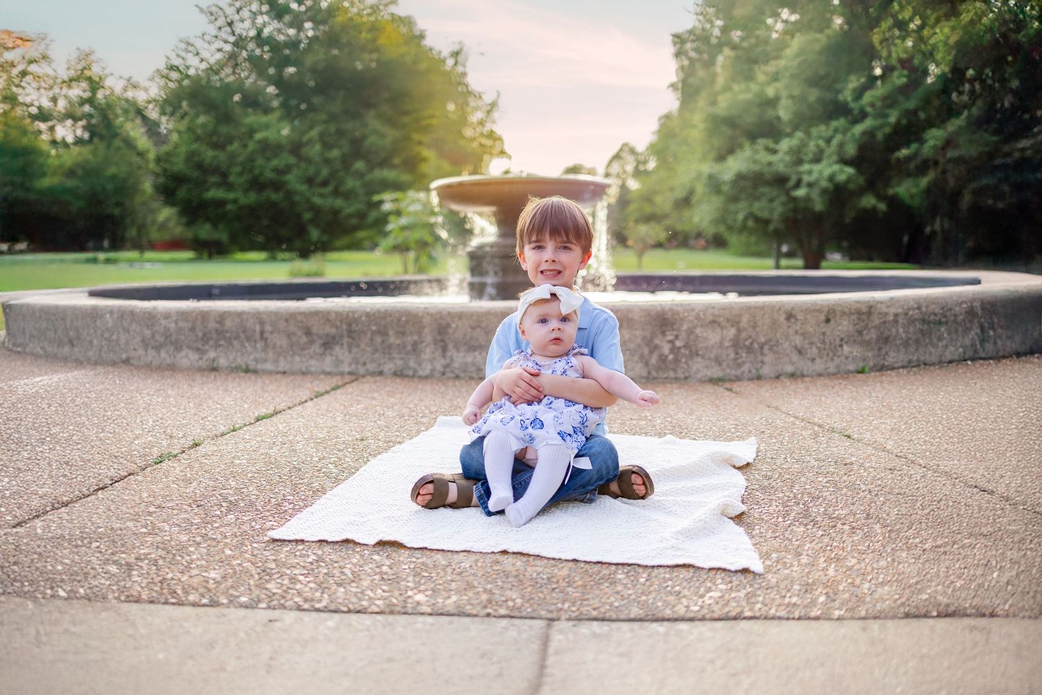 Central Illinois family photographer captures siblings sitting in front of a fountain with the sun setting in Springfield, IL