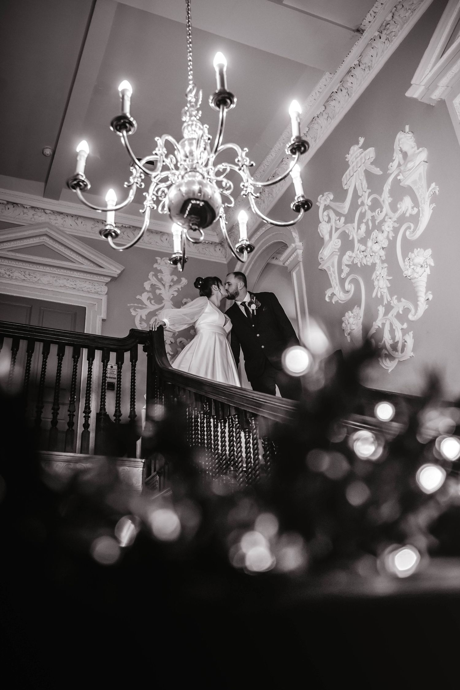 Romantic black and white photograph under an elegant crystal chandelier in a historic venue.