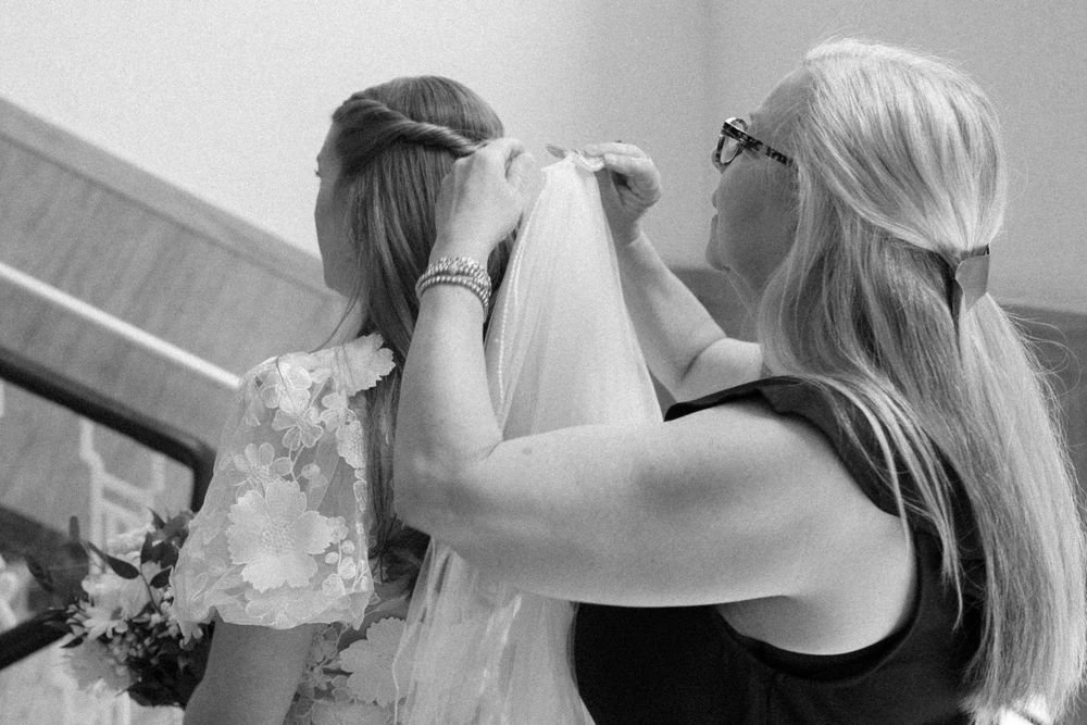 A black and white photograph shows final adjustments being made to a wedding veil during bridal preparations.