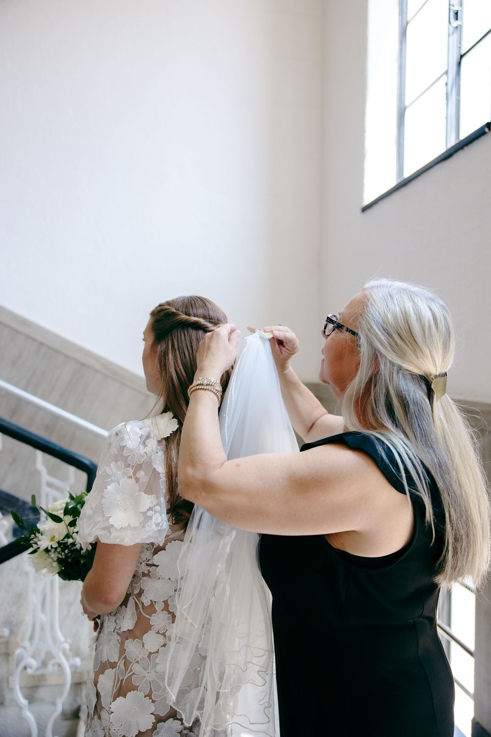 A wedding preparations scene shows the careful adjusting of a delicate lace veil in a bright, sunlit room.