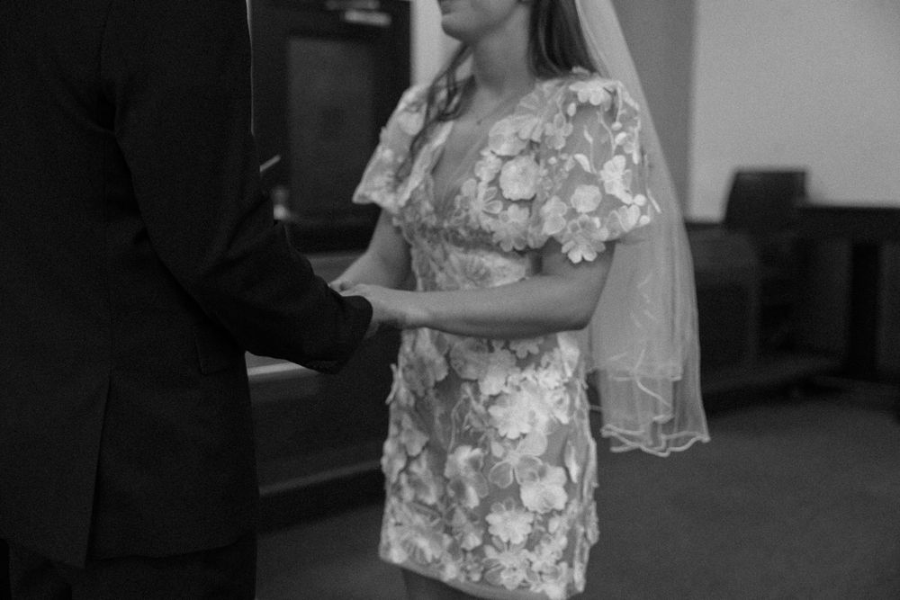 Black and white photo of a person wearing a floral print dress with lace details during what appears to be a ceremony.