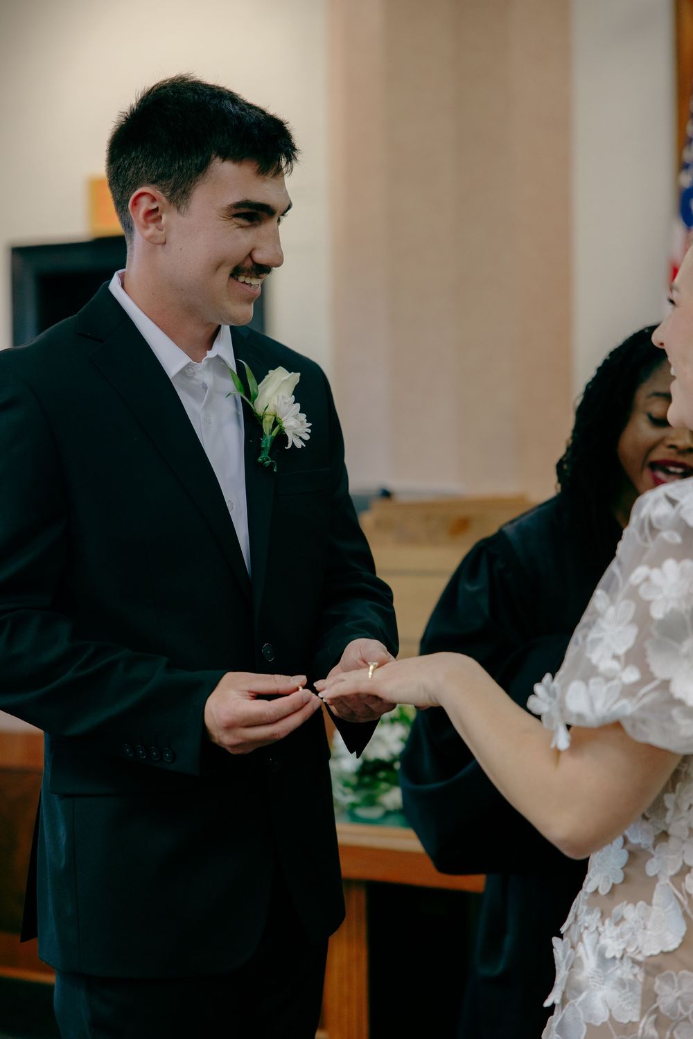 A couple exchanges rings during their wedding ceremony in a simple indoor venue with warm lighting.