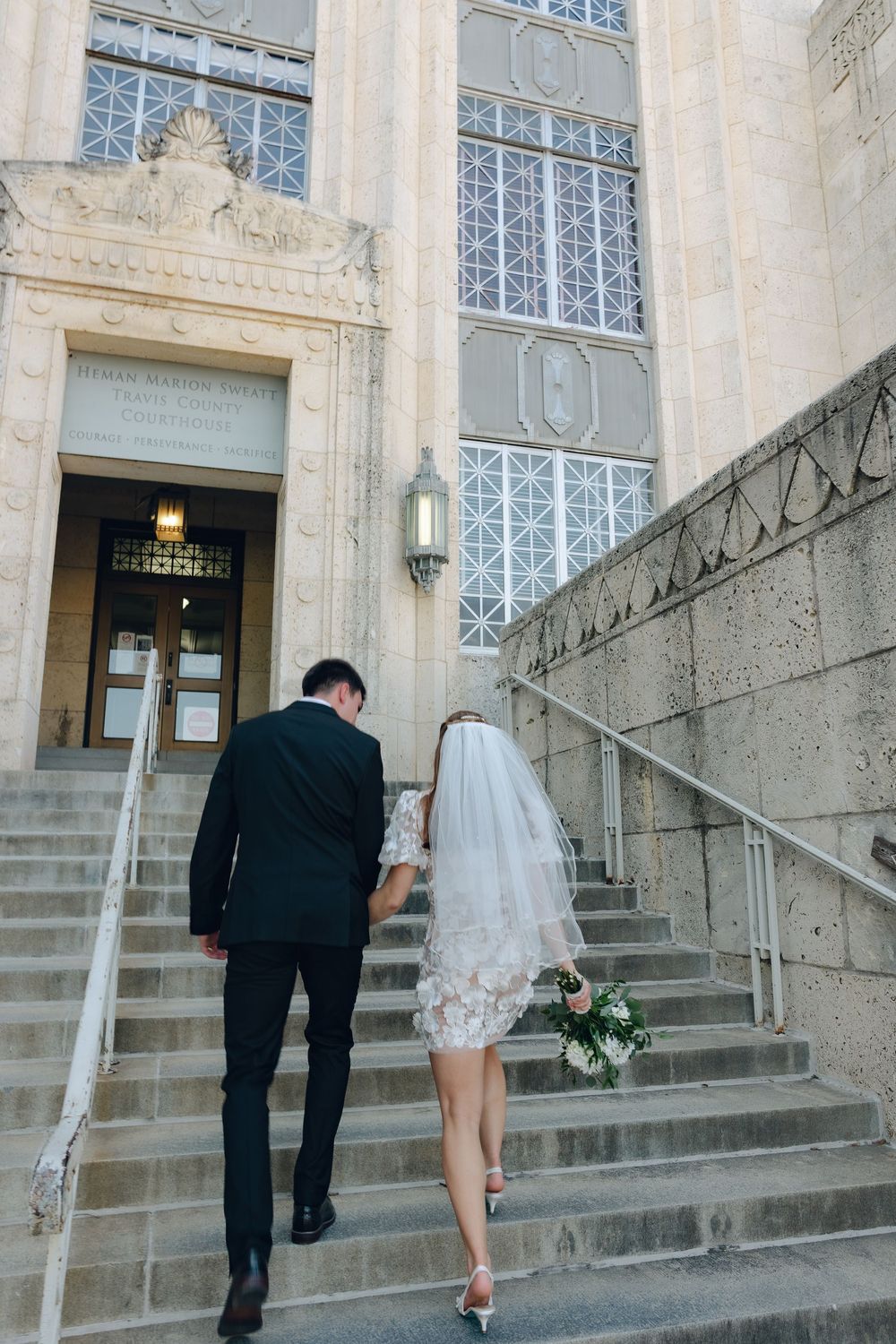 A couple ascending stone steps of a historic building with ornate windows and architecture.