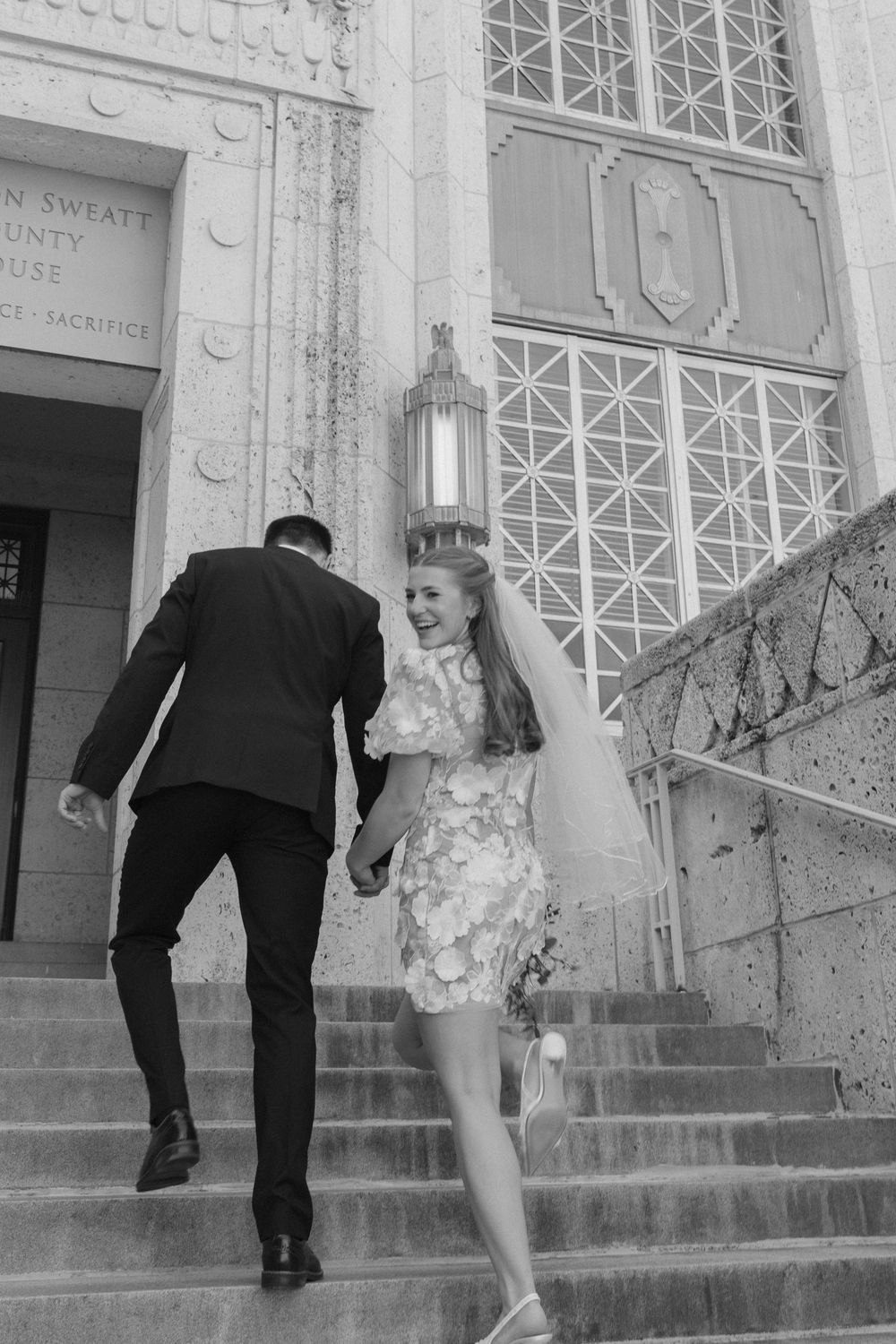 Black and white photo of newlyweds climbing steps at an elegant historic building entrance.