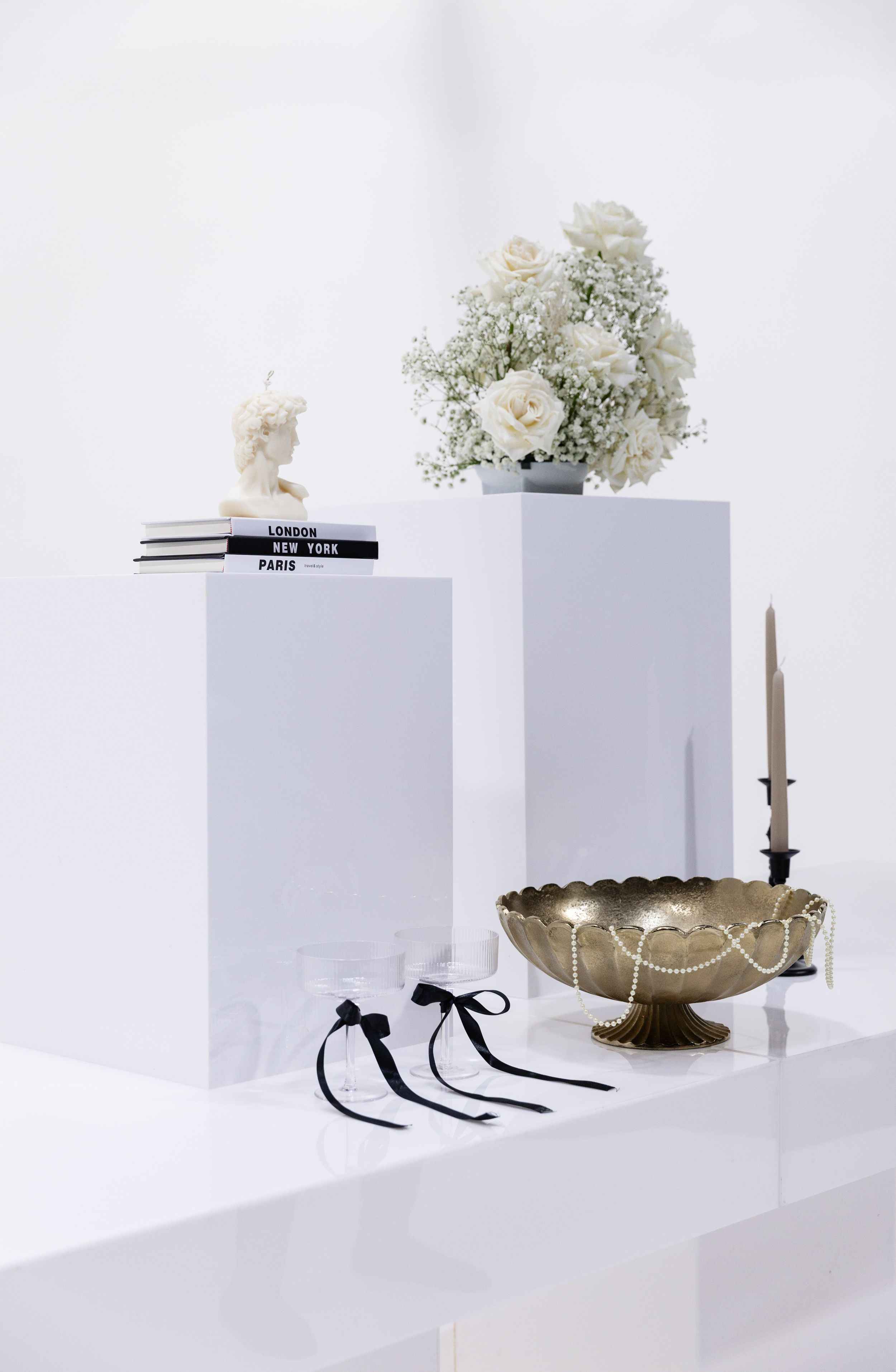 Minimalist white display pedestals with floral arrangements and decorative objects.