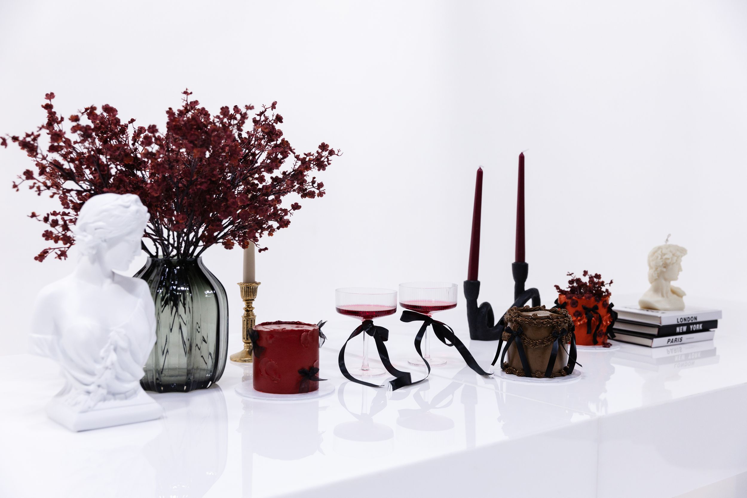 Artistic arrangement of deep red flowers and black vases on white platforms.
