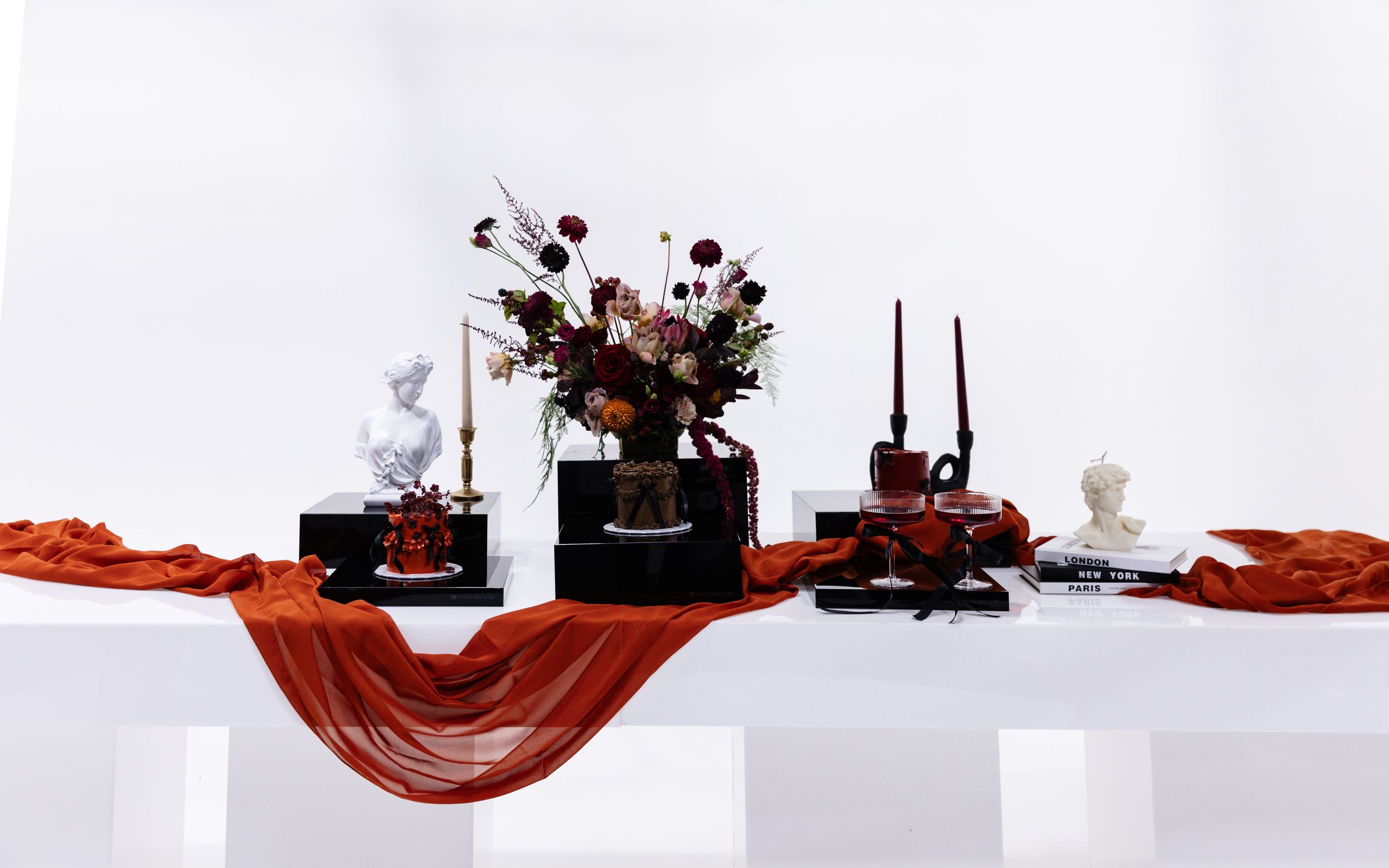 Modern table display with burgundy floral arrangements and white decorative elements.