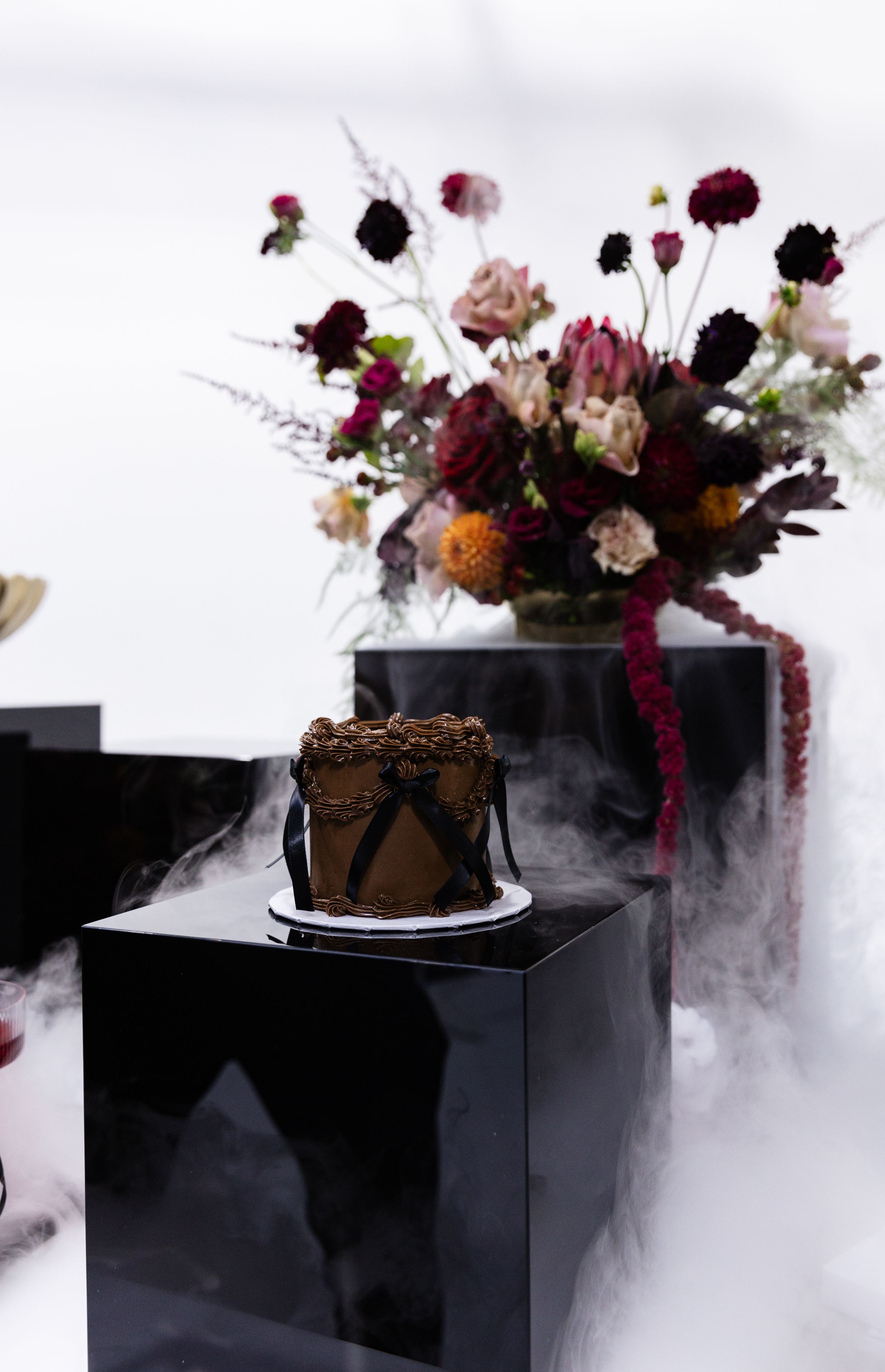 Dramatic dark display featuring burgundy flowers and black pedestals with misty atmosphere.