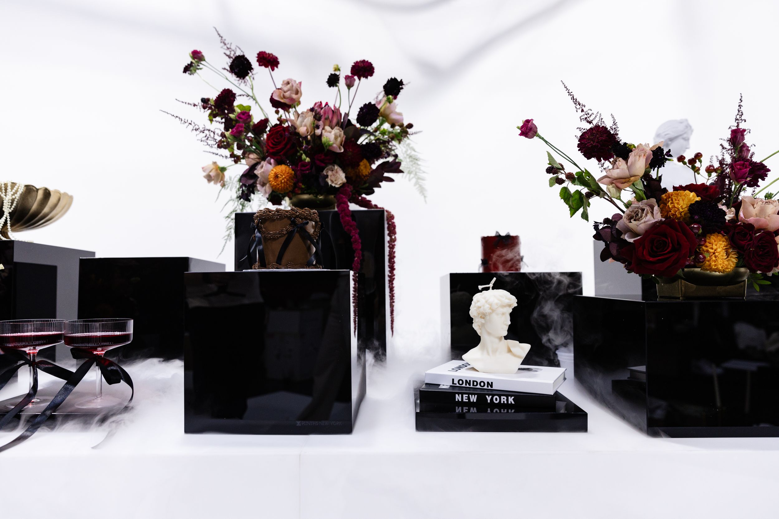 Moody arrangement of dark flowers and decorative objects on black platforms.