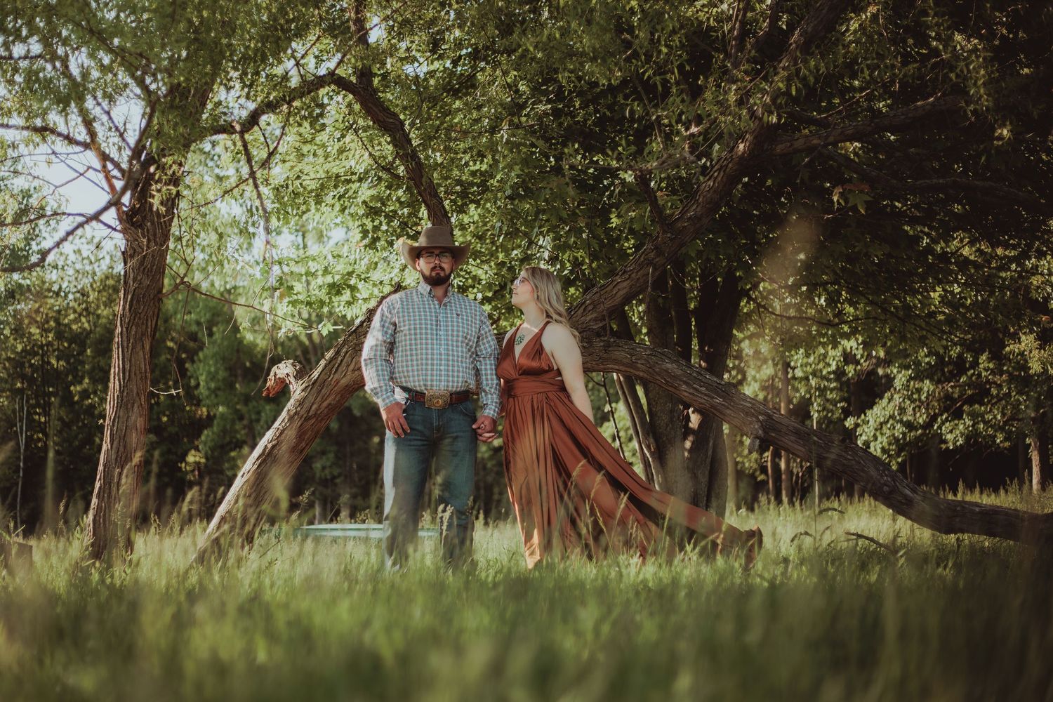 Couple embracing in a golden field at sunset while surrounded by wildflowers in autumn.