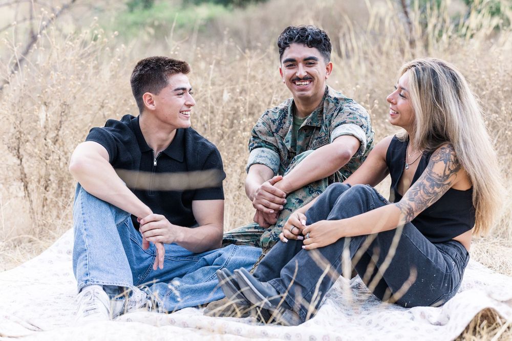 Three friends laugh and enjoy a relaxing afternoon together sitting on a blanket in a sunny field of dry grass.