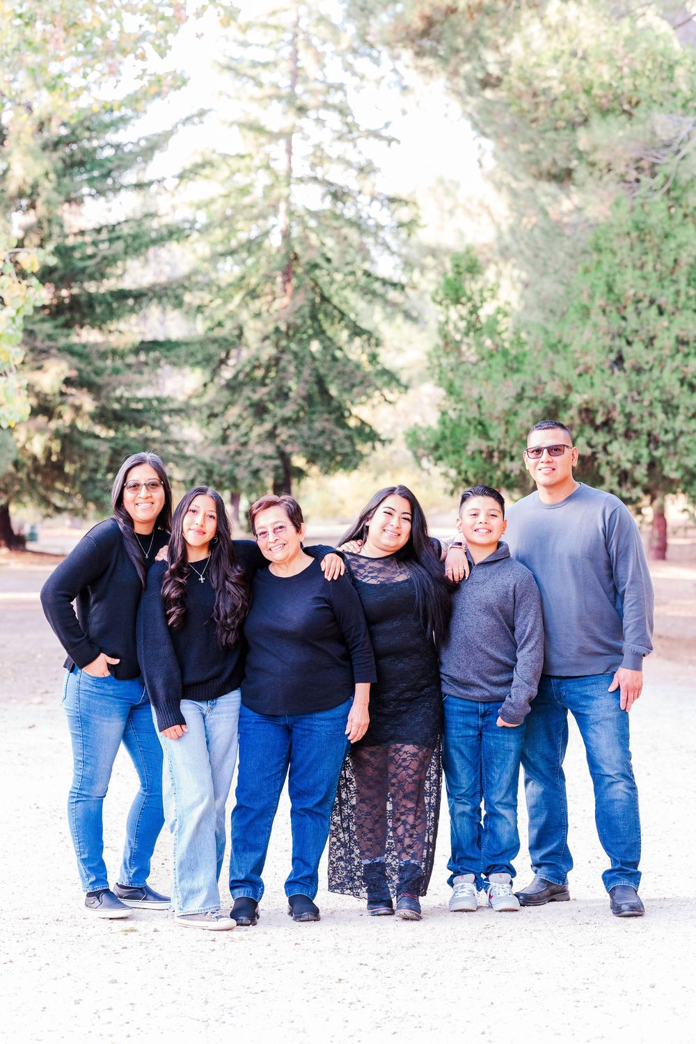 A group in coordinating blue and black outfits poses together outdoors with evergreen trees in the background.