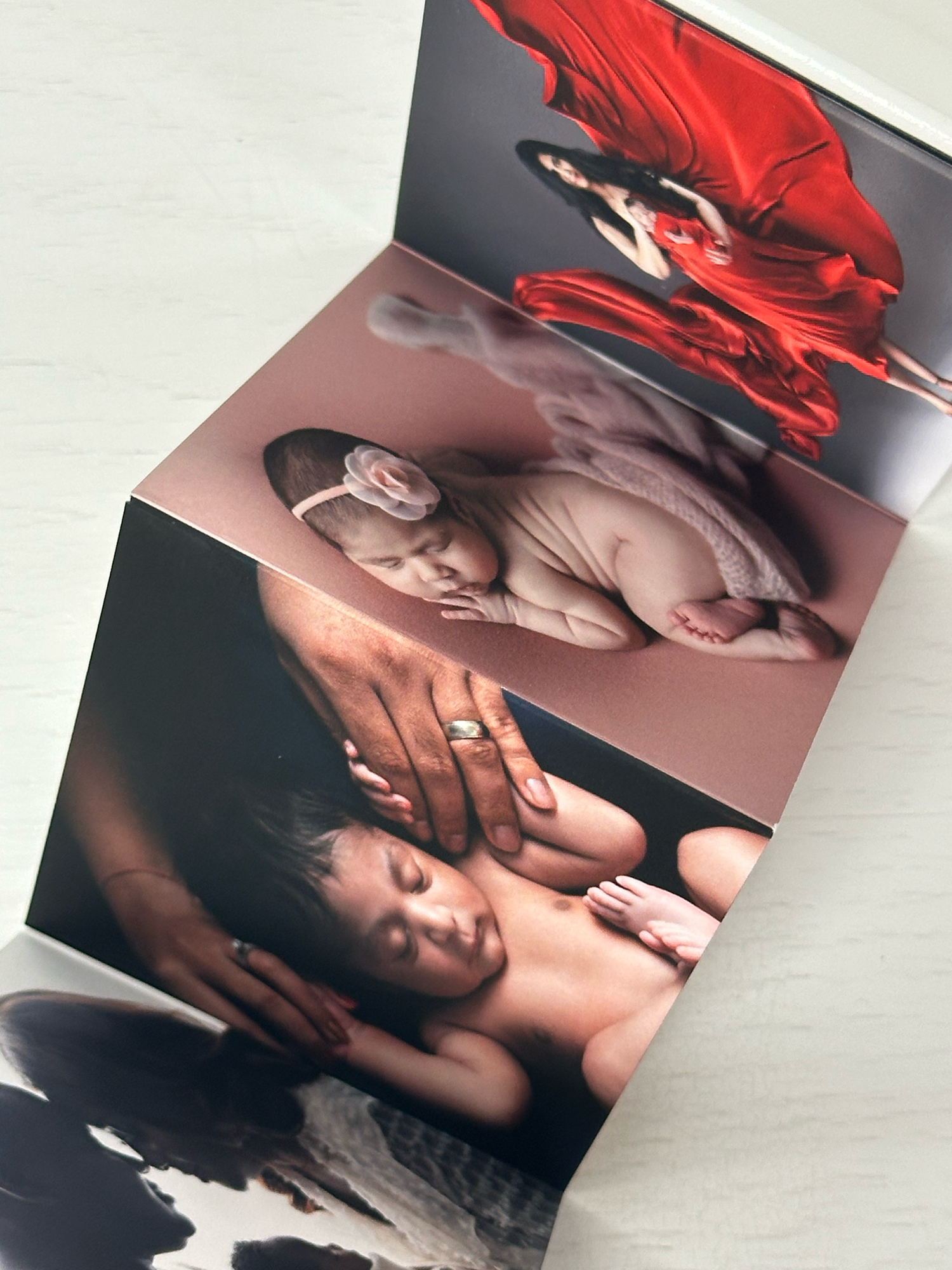 Open photo book displaying newborn, mother-baby bonding, and maternity photography sessions with vibrant red fabric.