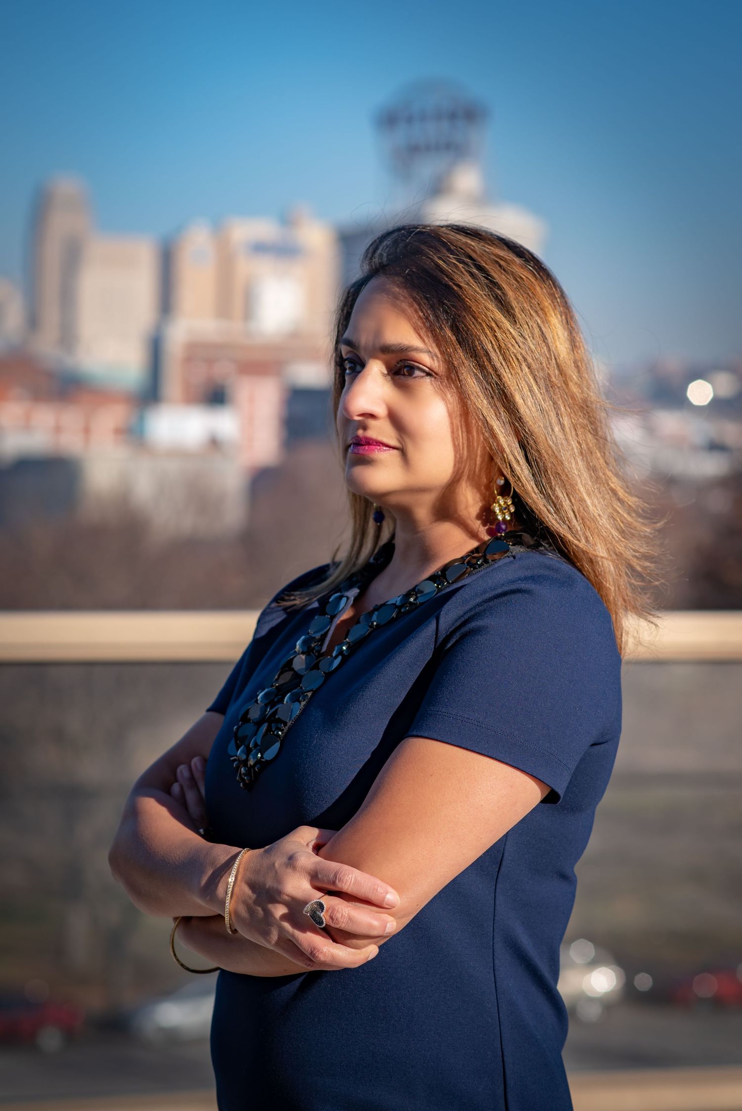 Professional woman in navy top with statement necklace against urban skyline.