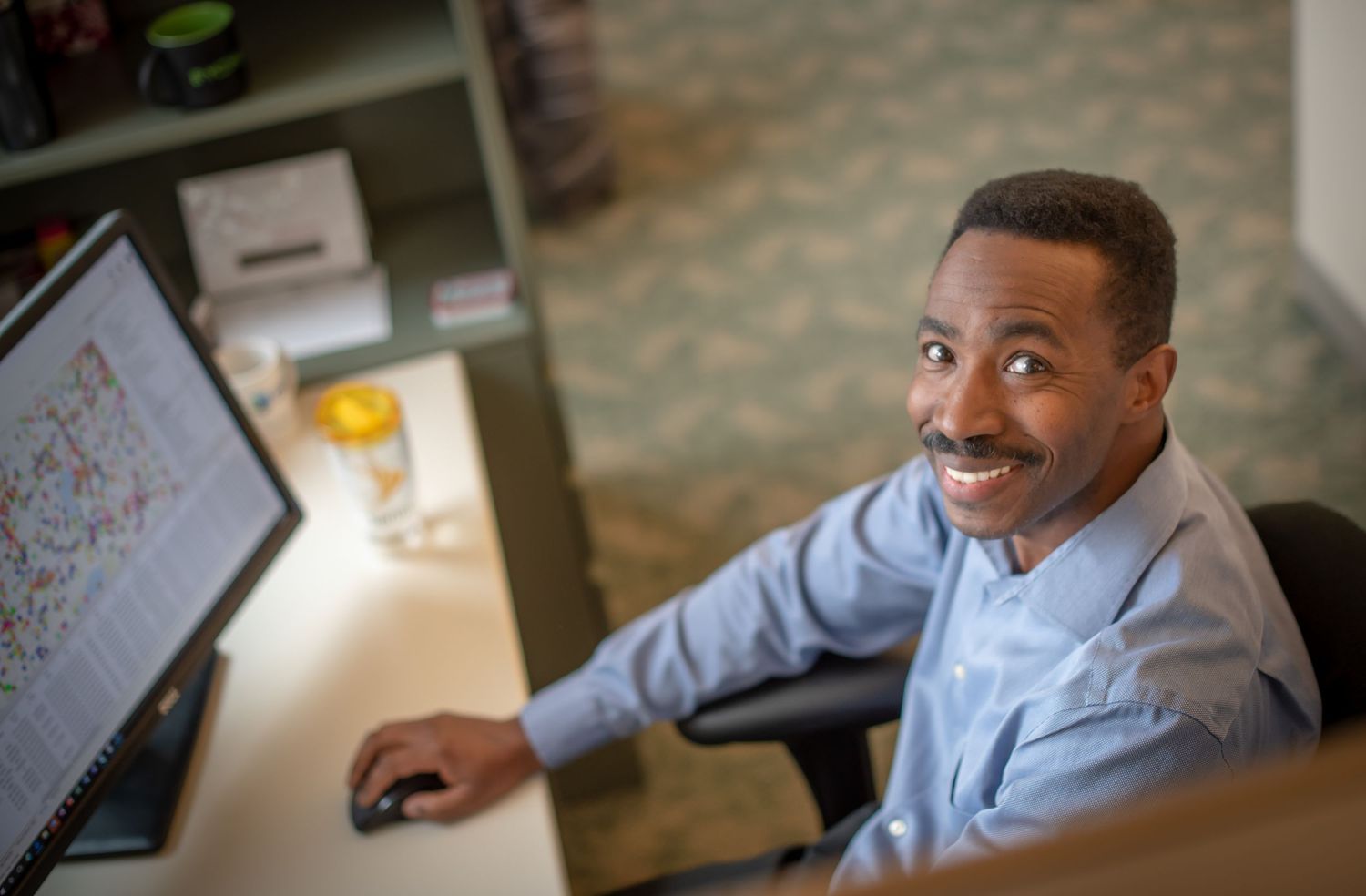 Professional working at a computer desk smiling while looking up at the camera.