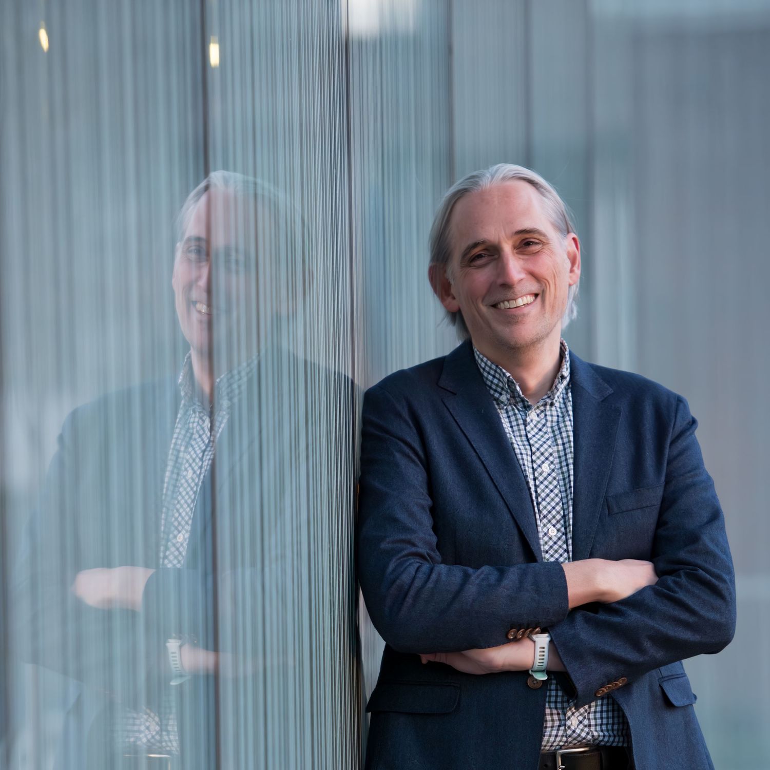 Professional portrait with reflection in glass wearing navy blazer and patterned shirt.