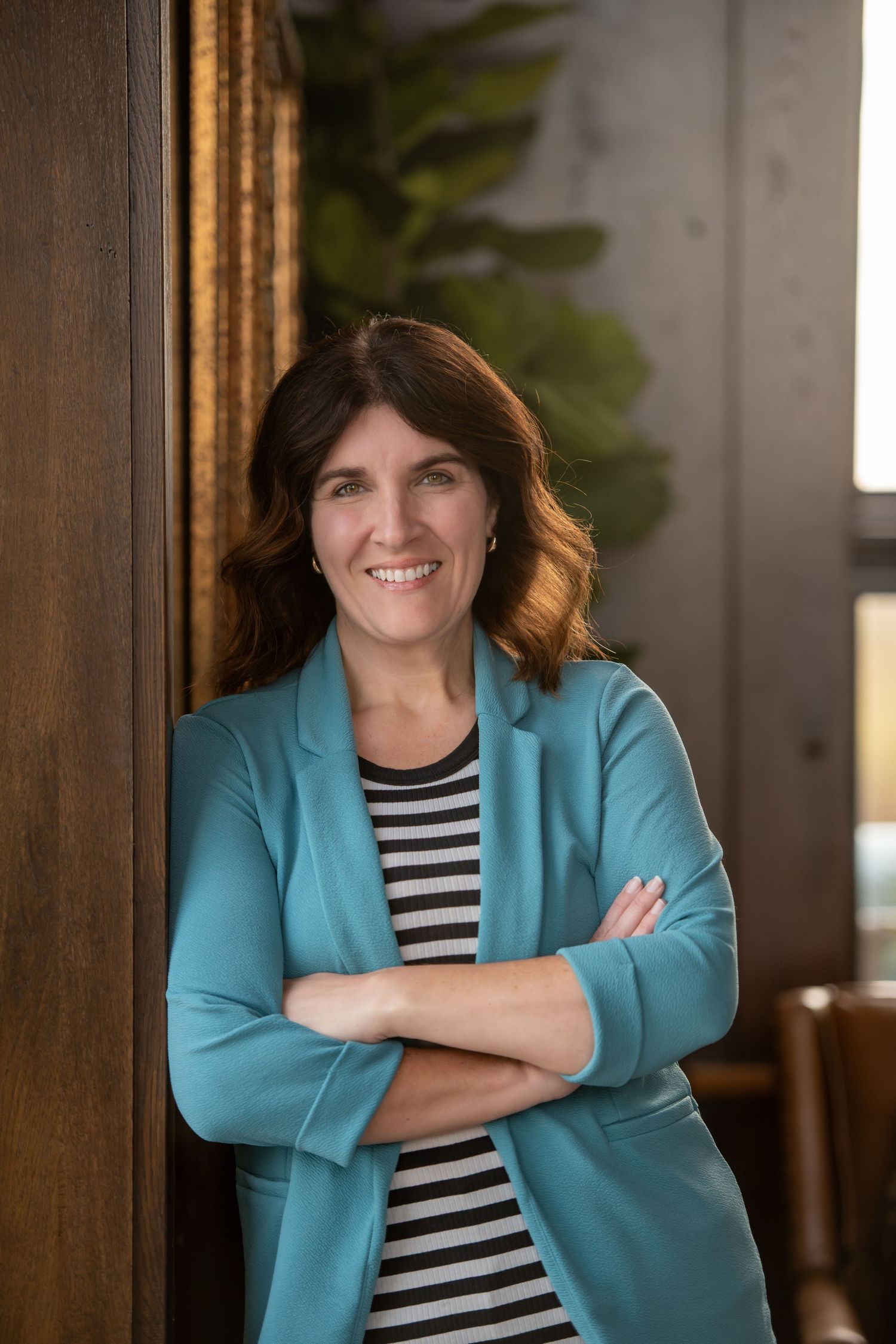 Professional woman in teal blazer crossing arms and smiling confidently.