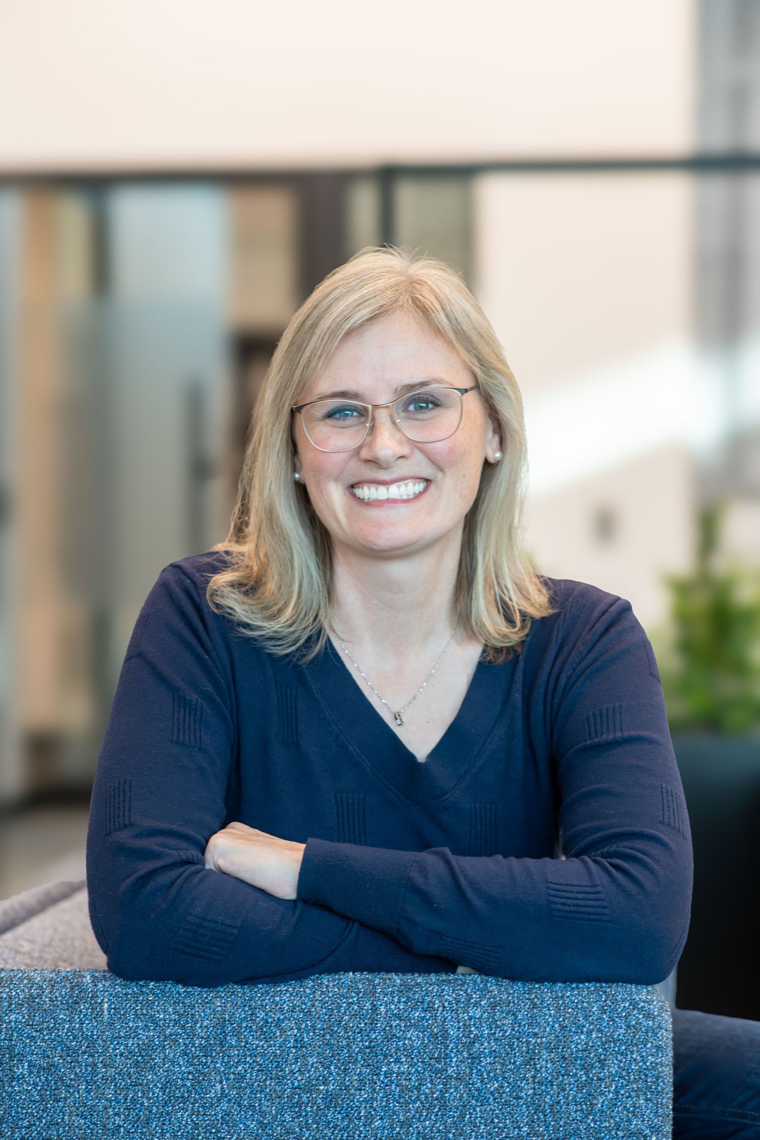 Woman in blue v-neck sweater smiling warmly while leaning on blue furniture.