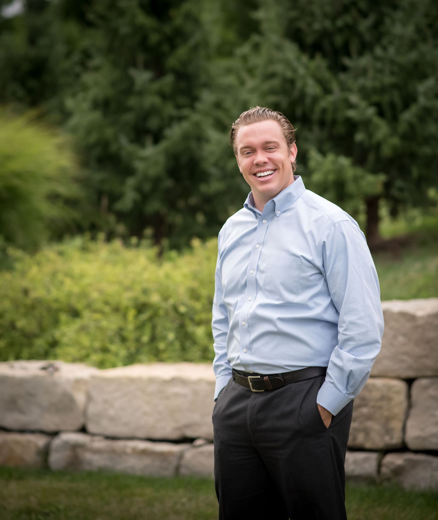 Professional outdoor portrait of doctor/dentist in business attire against a natural stone wall backdrop.