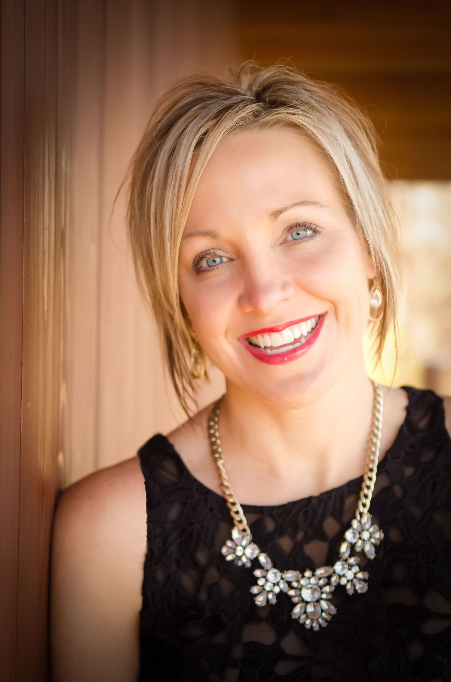 Elegant headshot featuring a black lace dress and statement crystal necklace against a warm background.