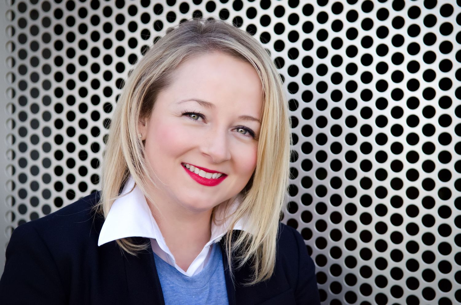 Corporate headshot against metallic perforated background with business attire and bright smile.