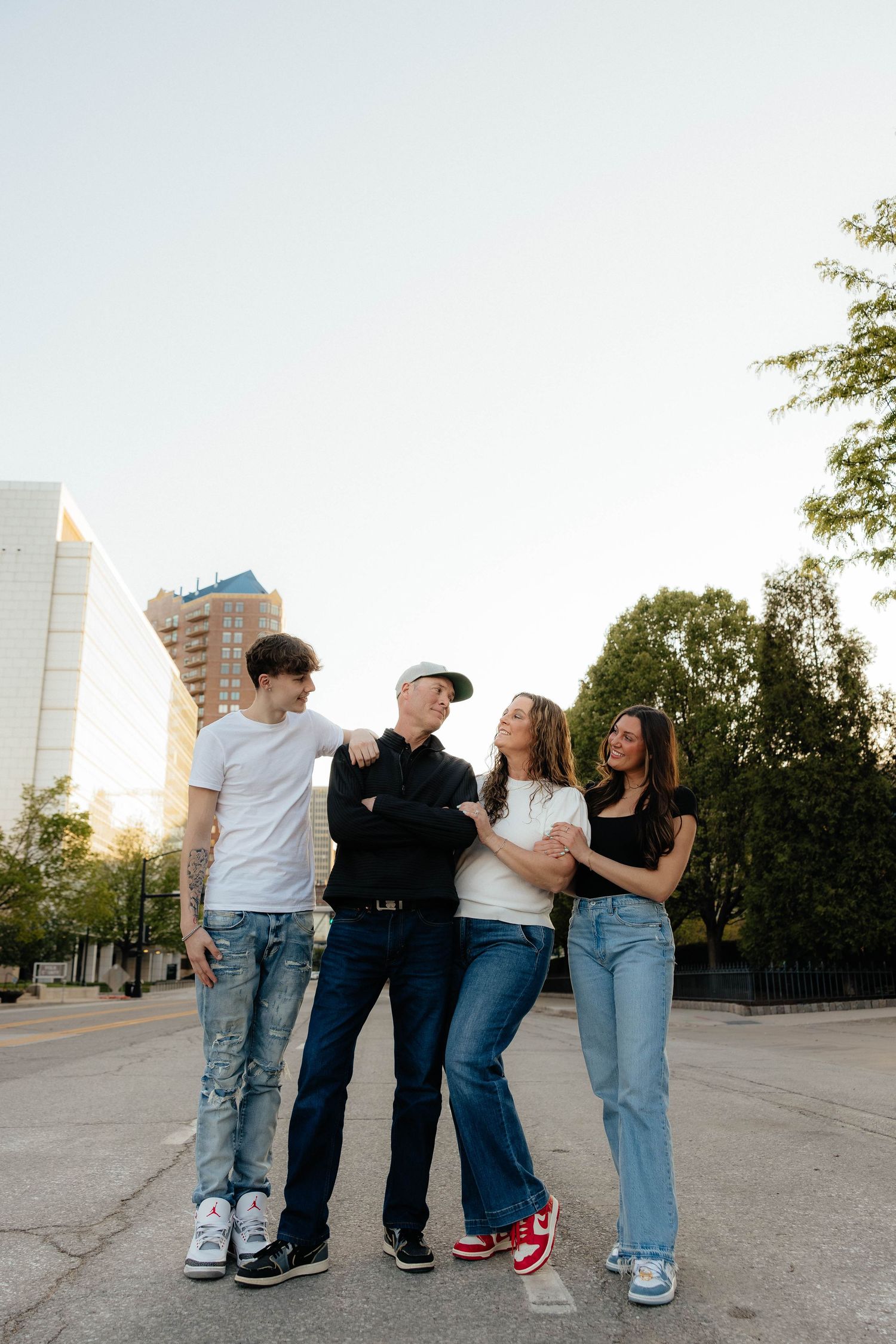 A small group stands together laughing and smiling on a city street at sunset with buildings in the background.