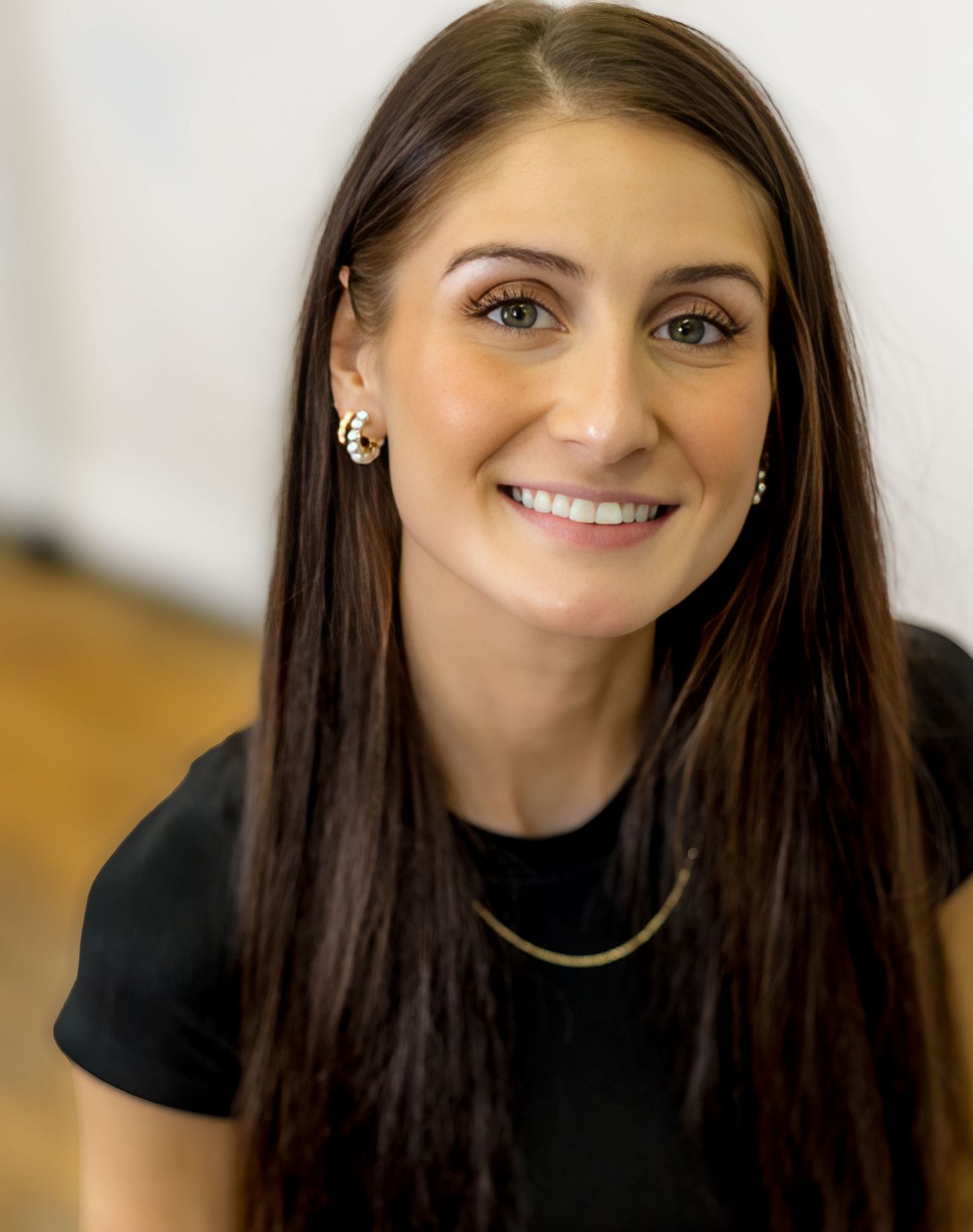Professional headshot of a person with long dark hair wearing a black top and delicate jewelry.