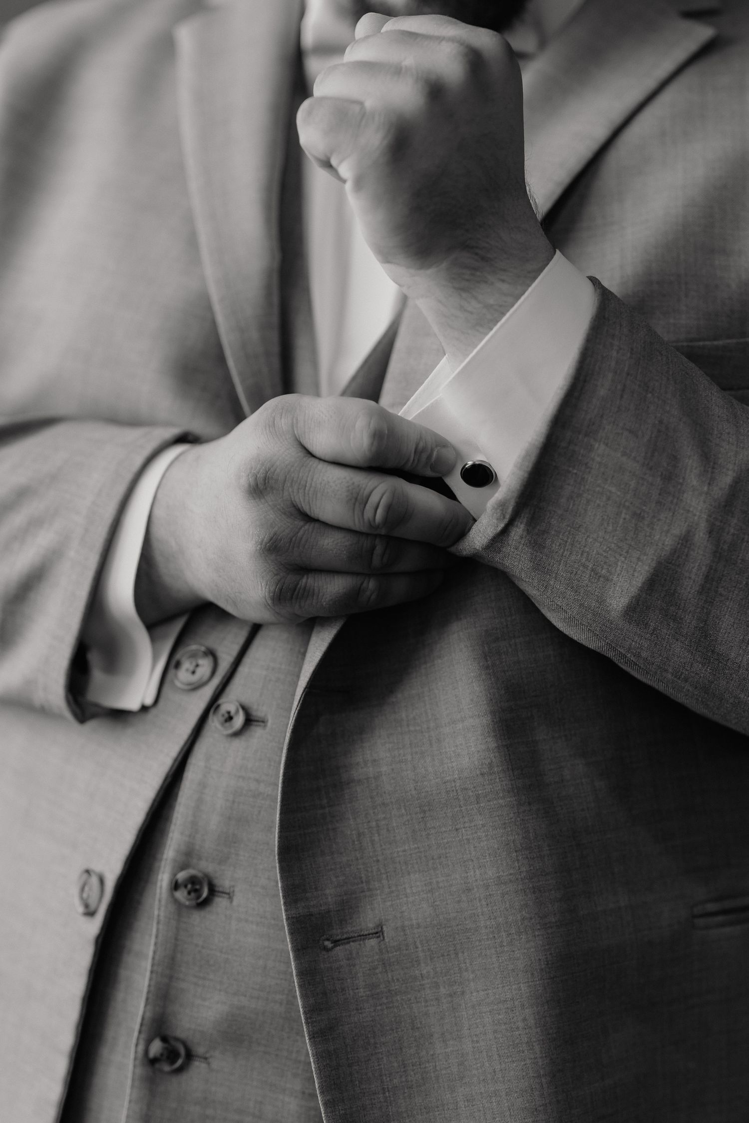 Close-up black and white photograph of a man adjusting his shirt cuff and buttons on his formal suit.