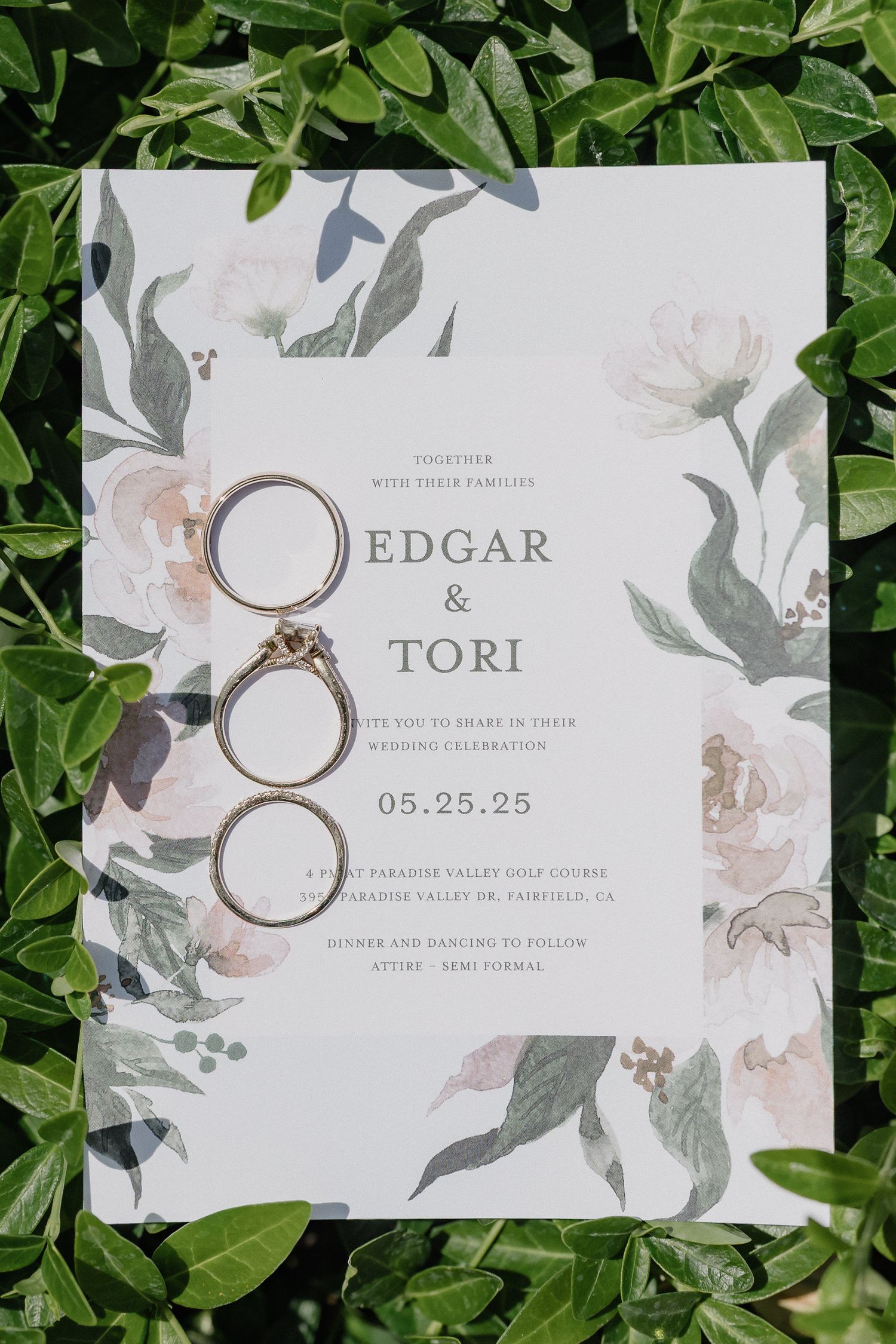 Elegant floral wedding invitation for Edgar and Tori with wedding rings photographed on green foliage background.