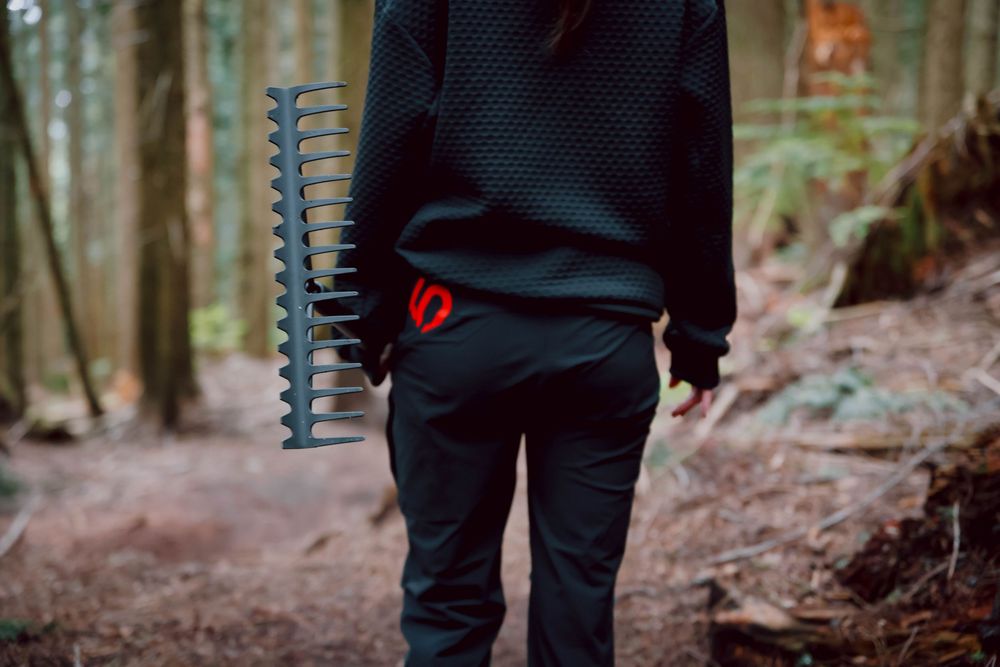 Spiral notebook held in front of dark clothing while standing on a forest trail surrounded by tall trees.