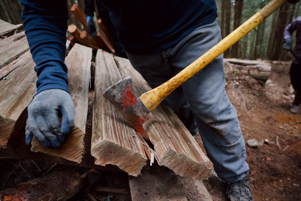 A gloved hand splits firewood with an axe on a wooden surface.