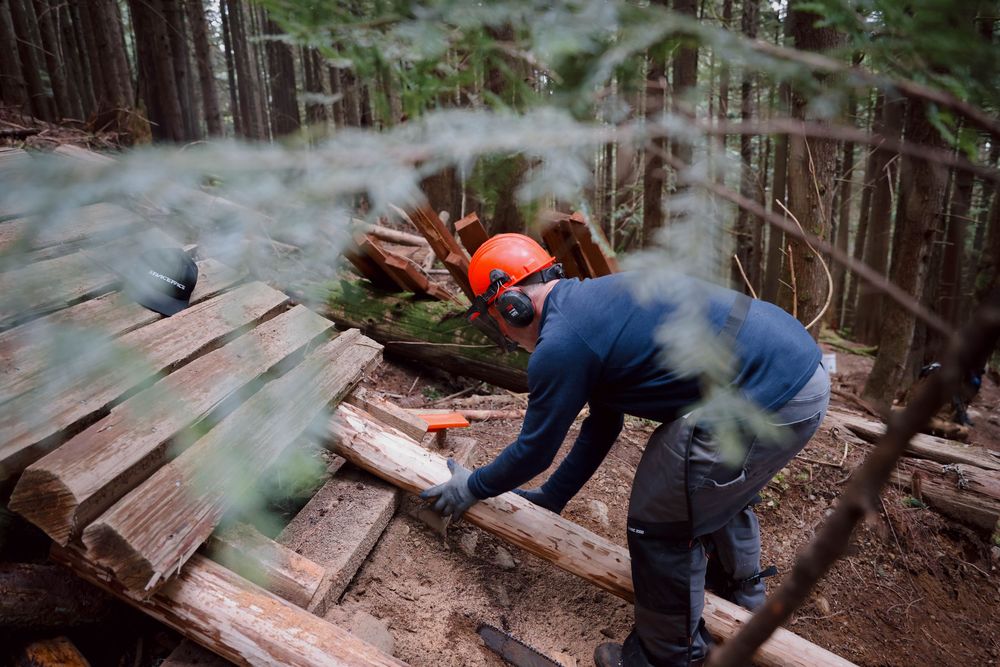 Mountain bike trail builder constructing wooden features on a forest trail using hand tools and lumber.