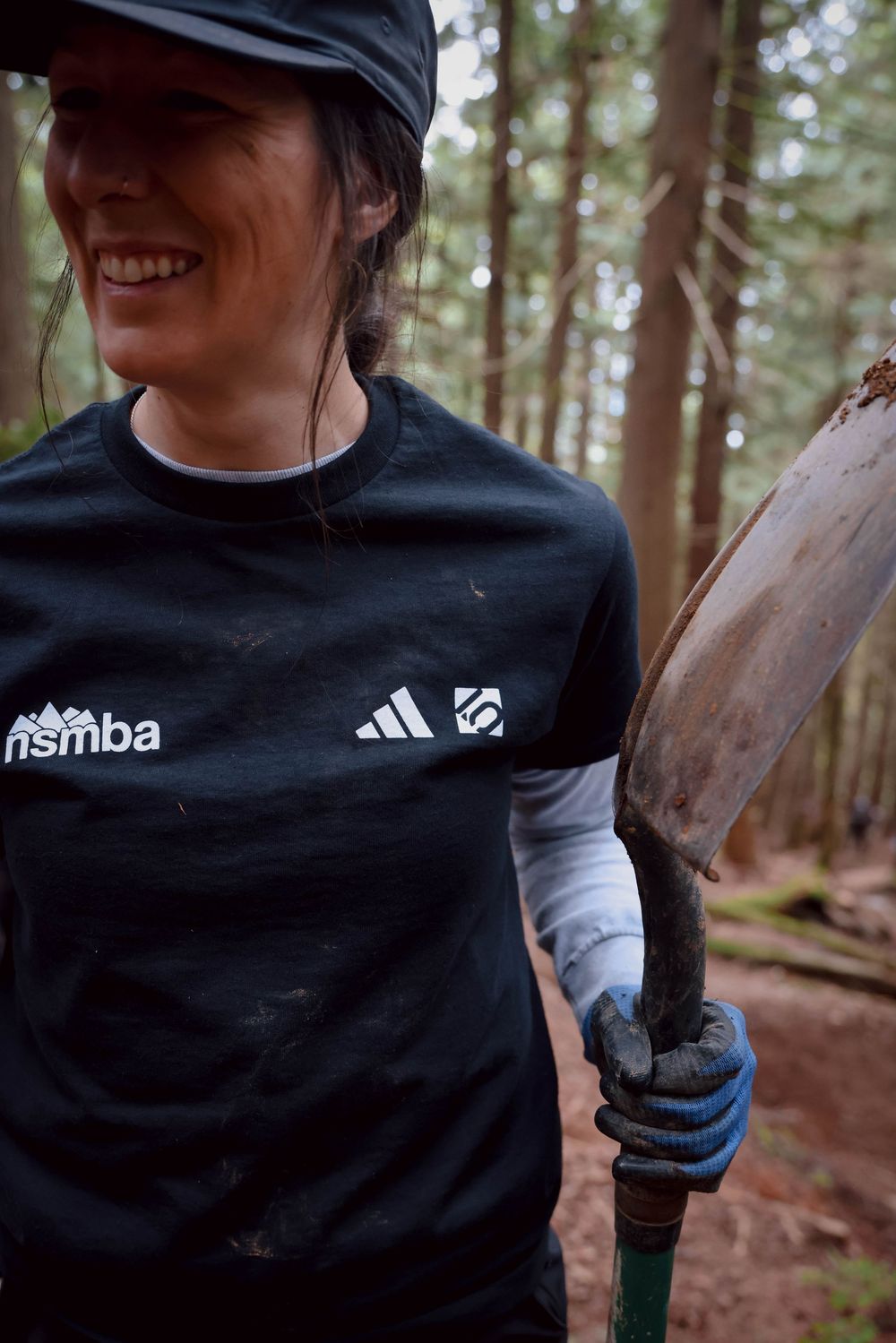 Mountain biker in black Asmba and Adidas jersey holds tool while riding on forest trail.