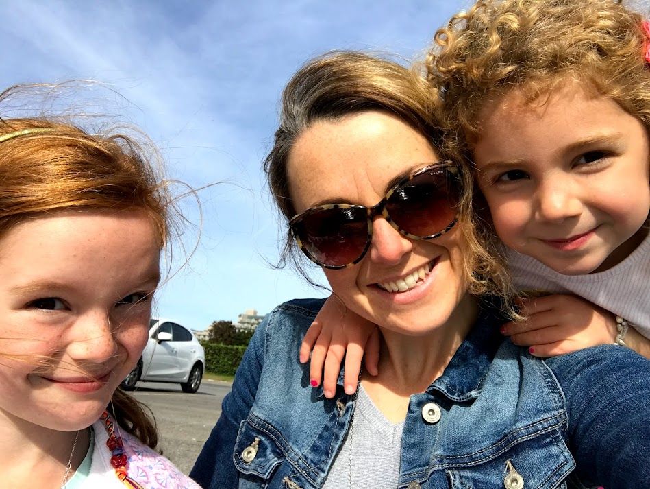 Three people in denim jackets pose together for a sunny outdoor selfie on a bright day.