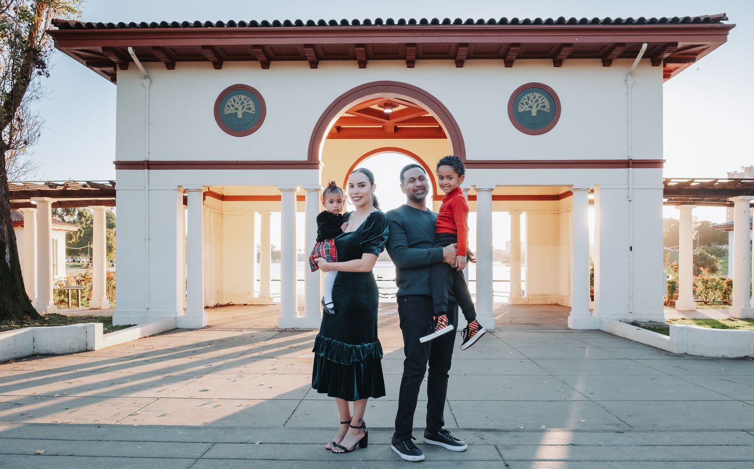 A couple stands in a dance pose together in front of a white Spanish-style archway entrance.
