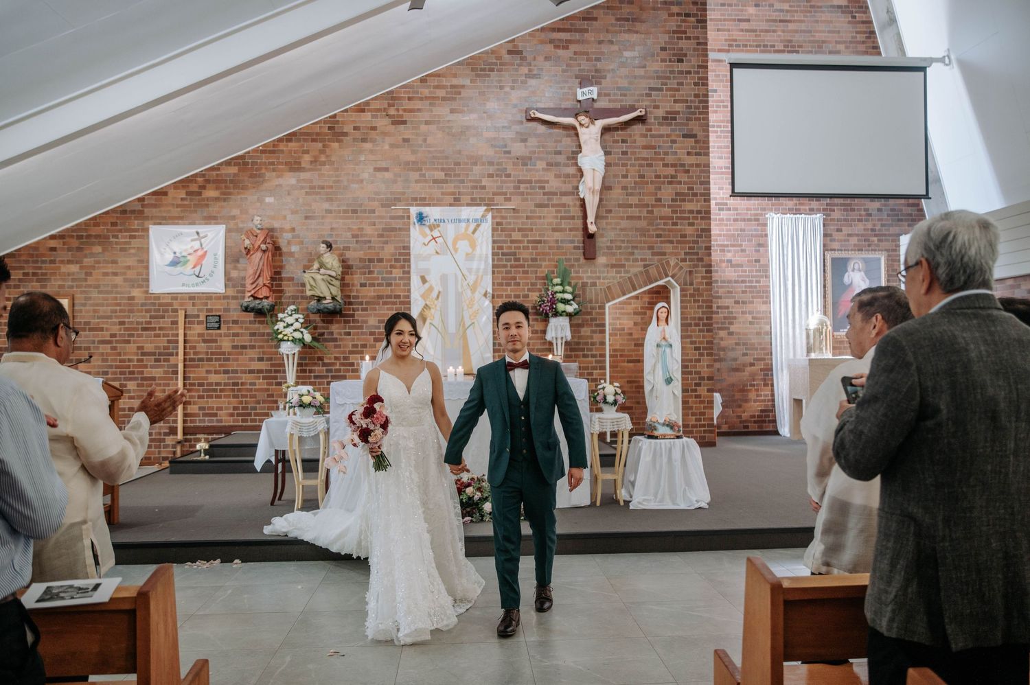 Newlywed couple joyfully walks down church aisle with exposed brick walls and religious decor during wedding ceremony.