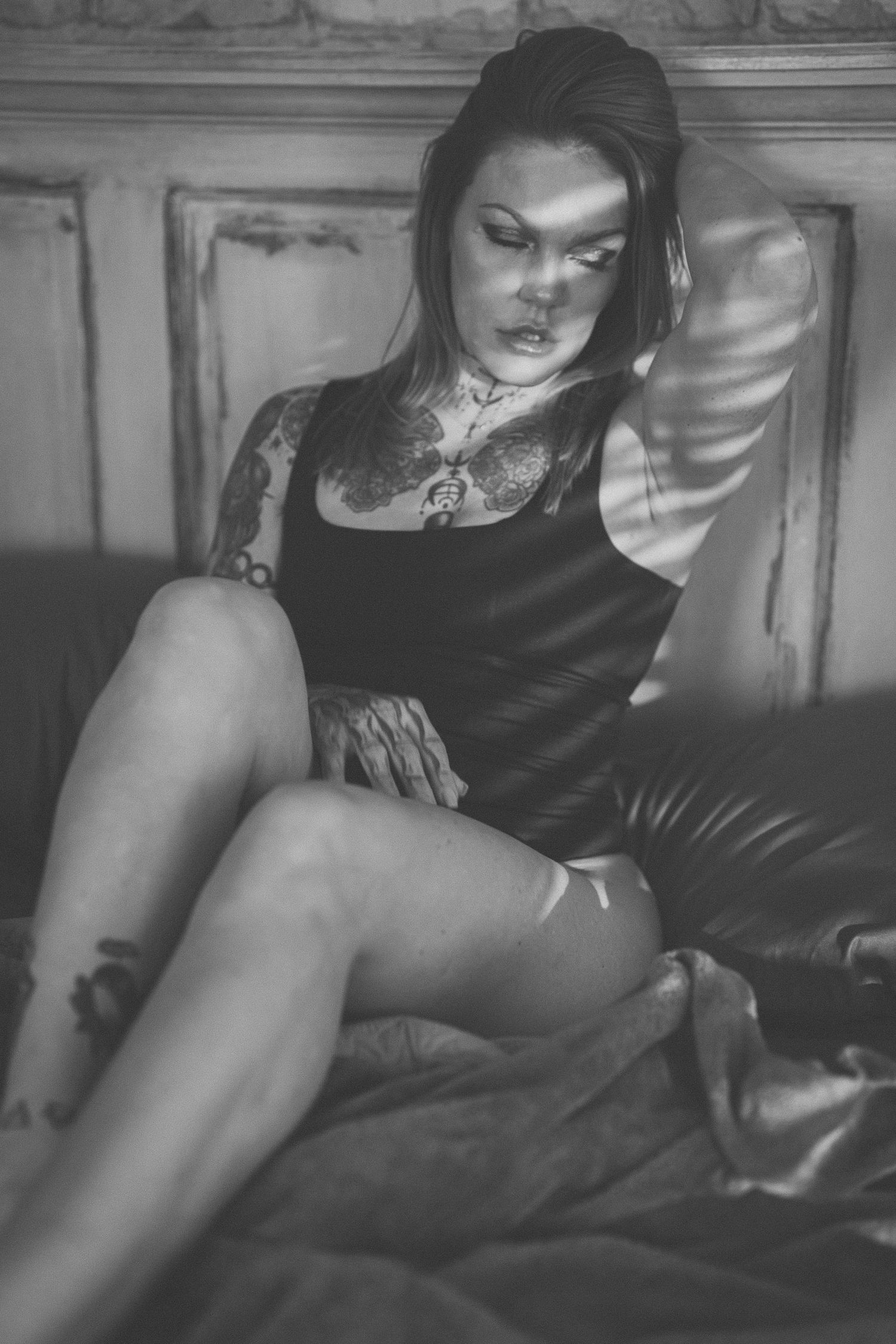 Dramatic black and white portrait of a model in dark clothing reclining on a vintage couch with moody shadows.