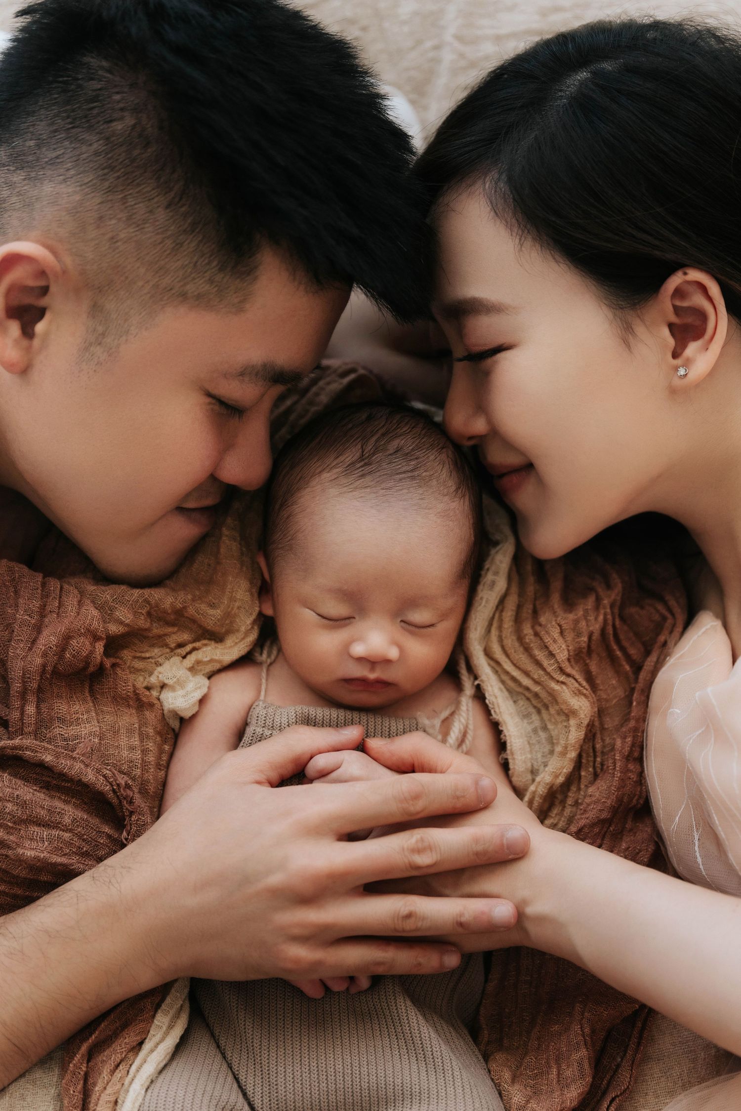 Tender close-up photo series showing parents lovingly embracing their newborn baby in warm brown tones.