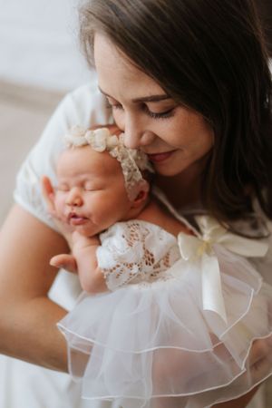 Mother and baby share tender moments in soft lighting while wearing delicate white lace and tulle clothing.