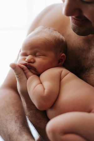 A tender close-up of a parent gently cradling and kissing a sleeping newborn baby.
